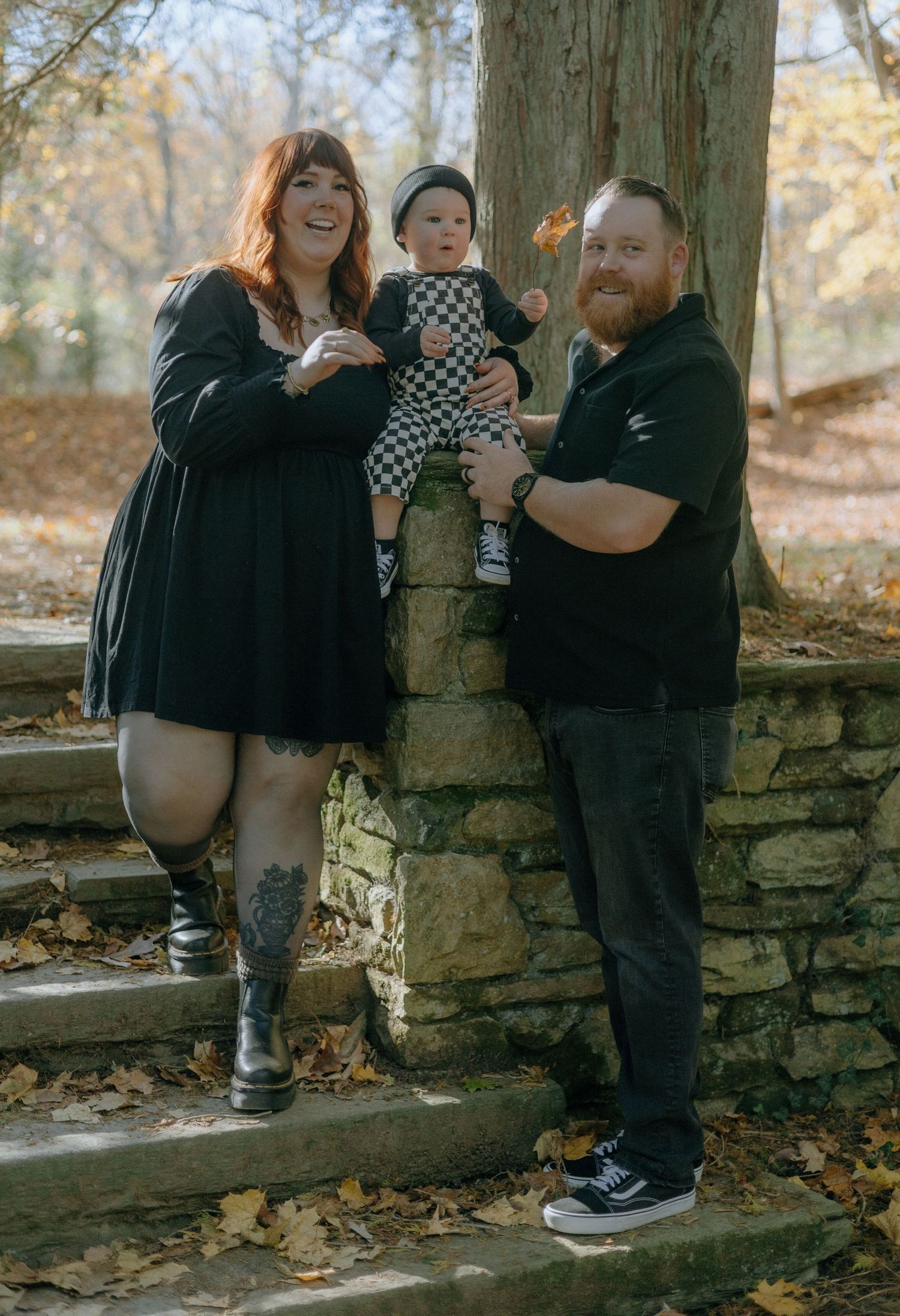 Family enjoying autumn moments together while sitting on a rustic stone wall surrounded by fallen leaves.