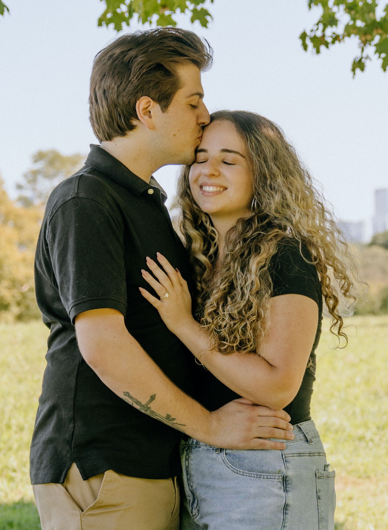 Affectionate moment captured between couple during outdoor photoshoot in sunny field.