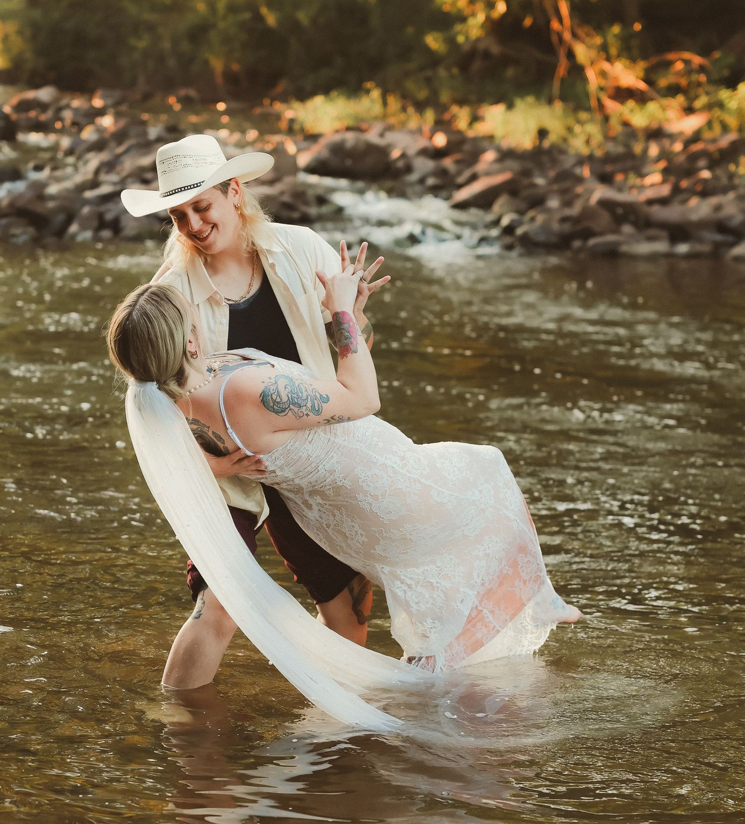 A romantic dip in the river during a wedding photoshoot with golden sunlight filtering through trees.