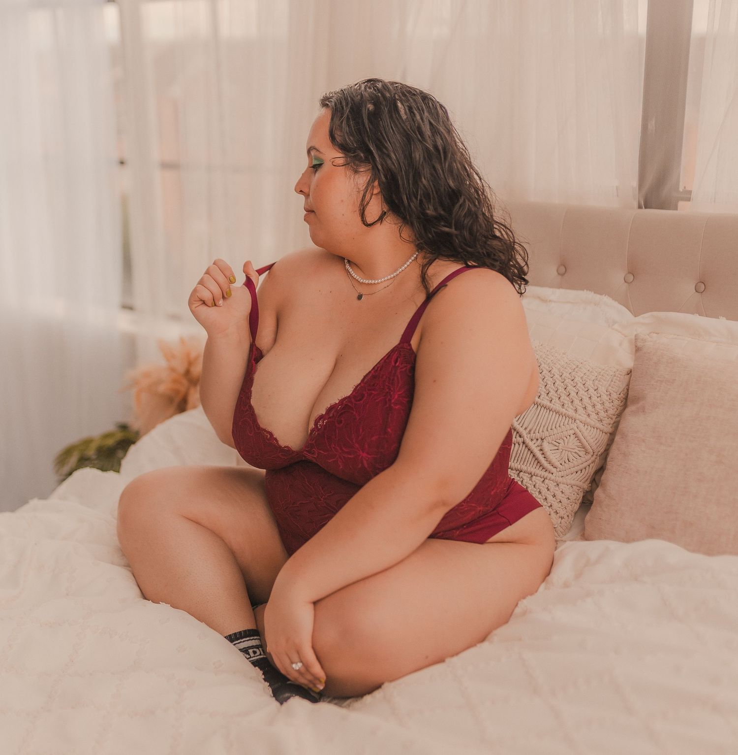 Romantic boudoir photography featuring burgundy lingerie on white bedding.