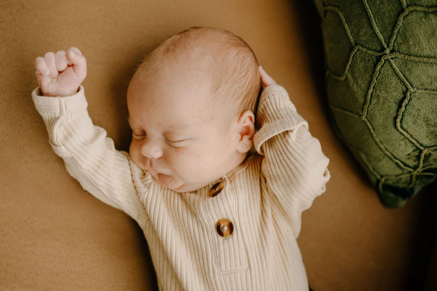 A baby wearing a cream knit sweater lies on a brown surface with decorative green accents.
