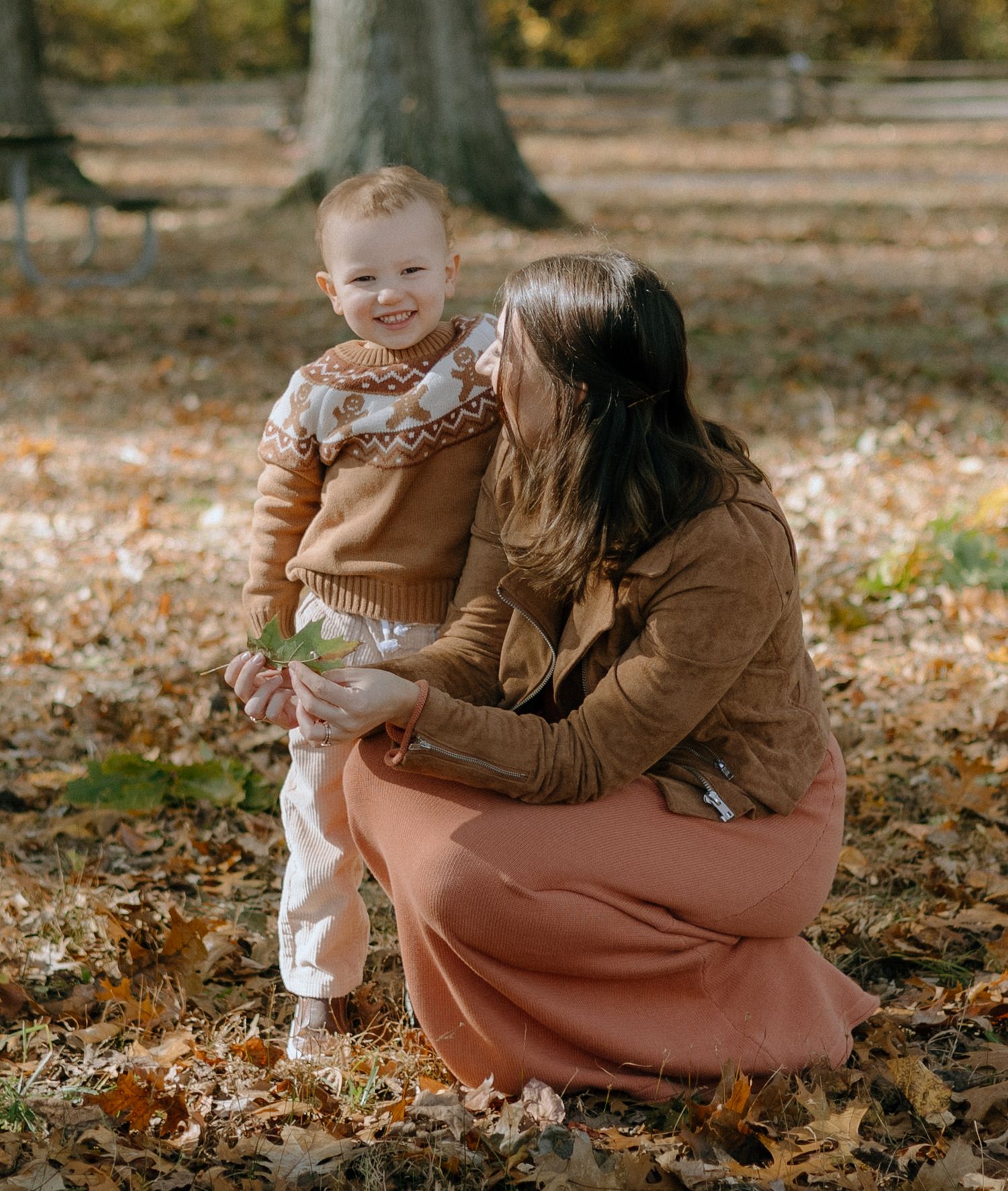 A parent and child play together in fallen autumn leaves on the ground during a fall photo session.