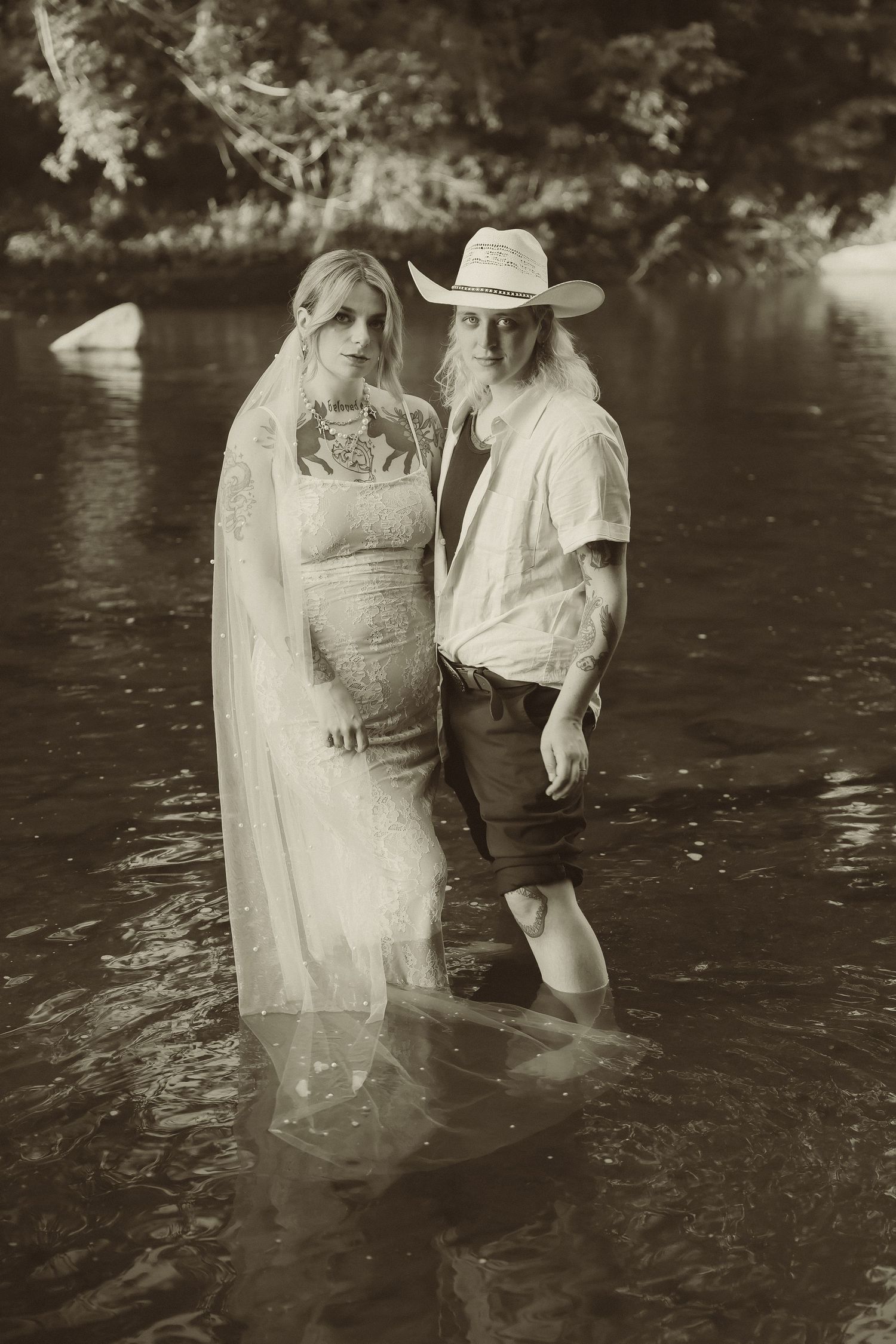 A black and white wedding portrait of two people standing in a serene river setting.