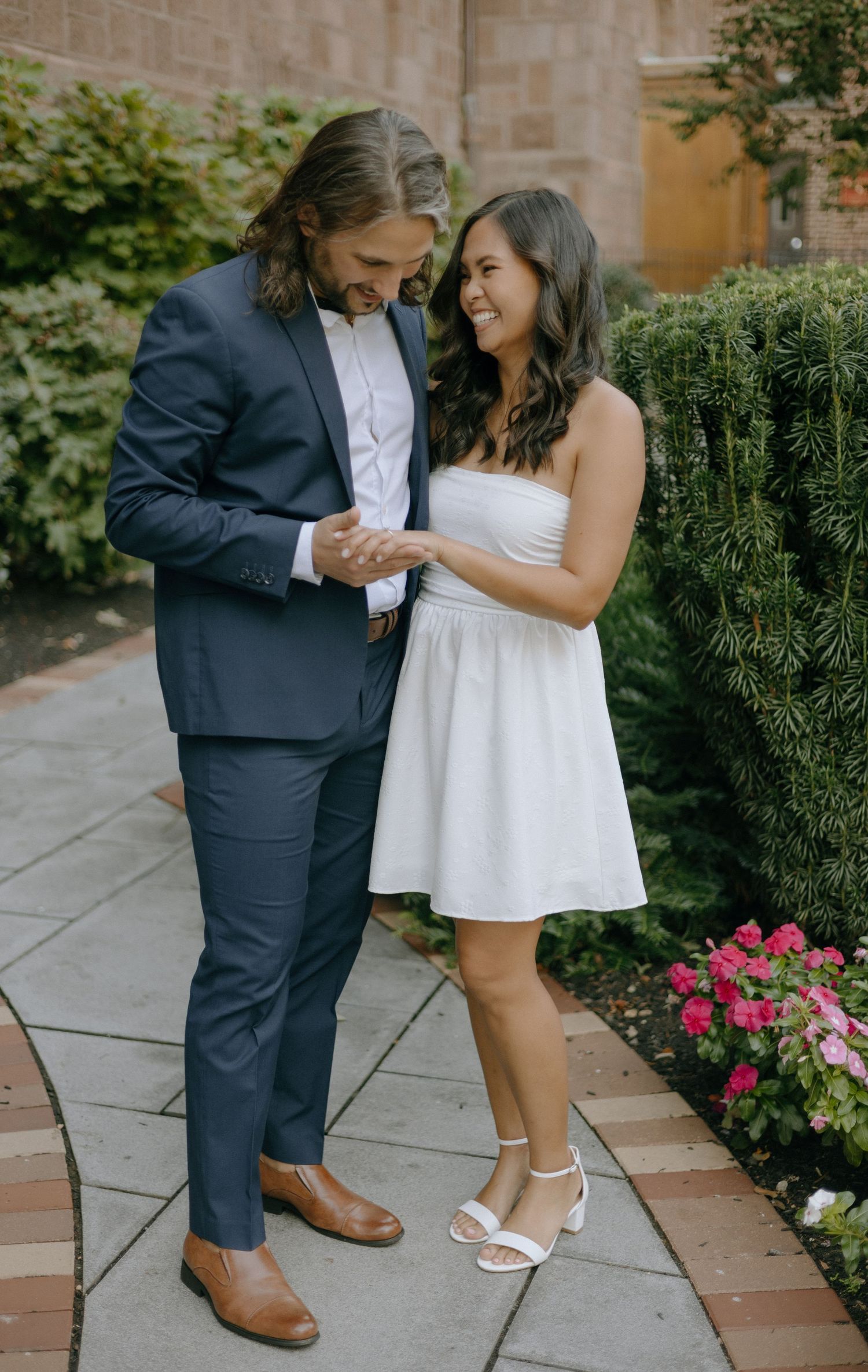 A romantic couple shares an intimate moment on a stone patio with pink flowers in the background.