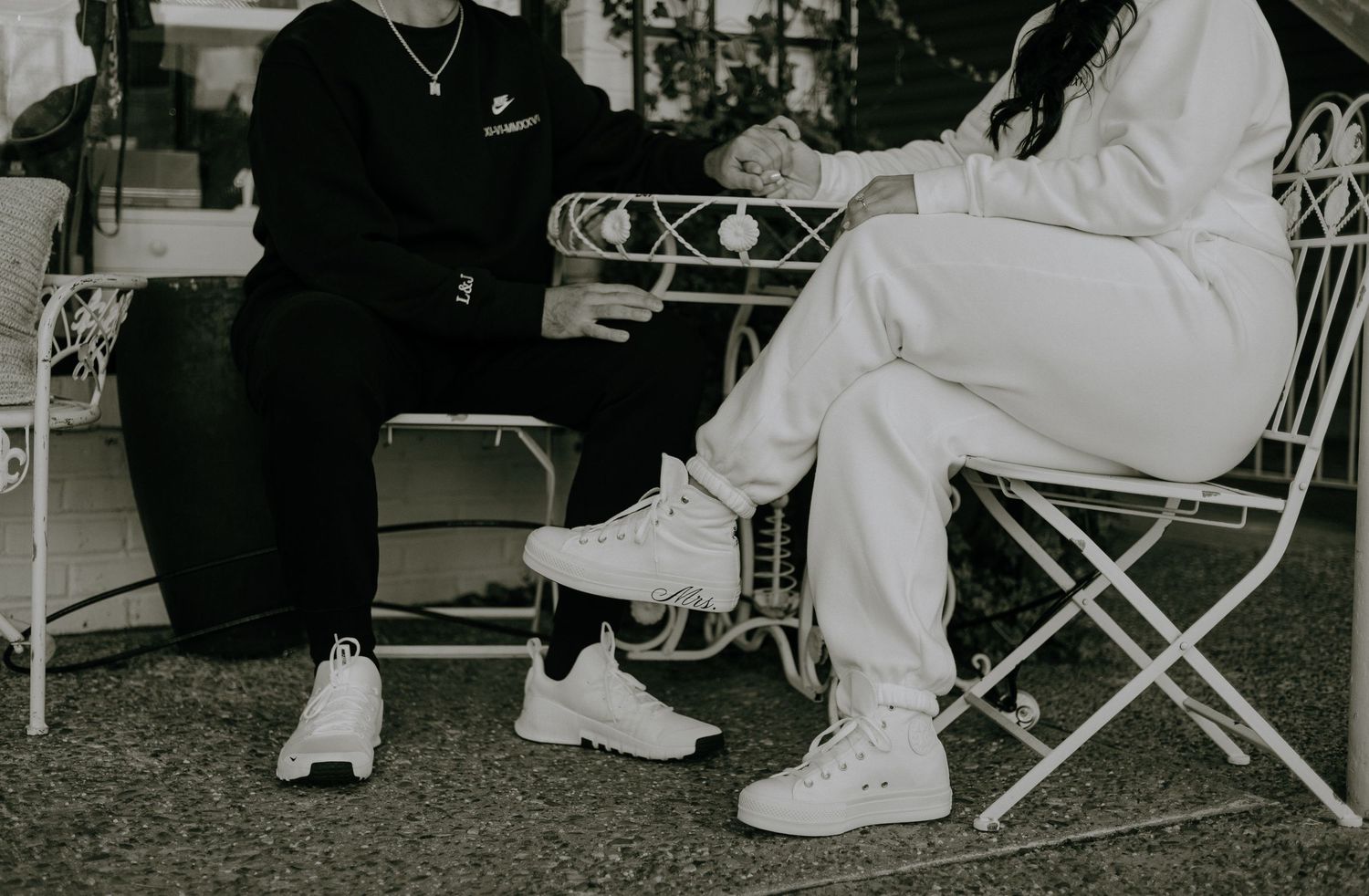Black and white photograph showing people sitting in folding chairs at an outdoor event wearing white shoes and clothing.