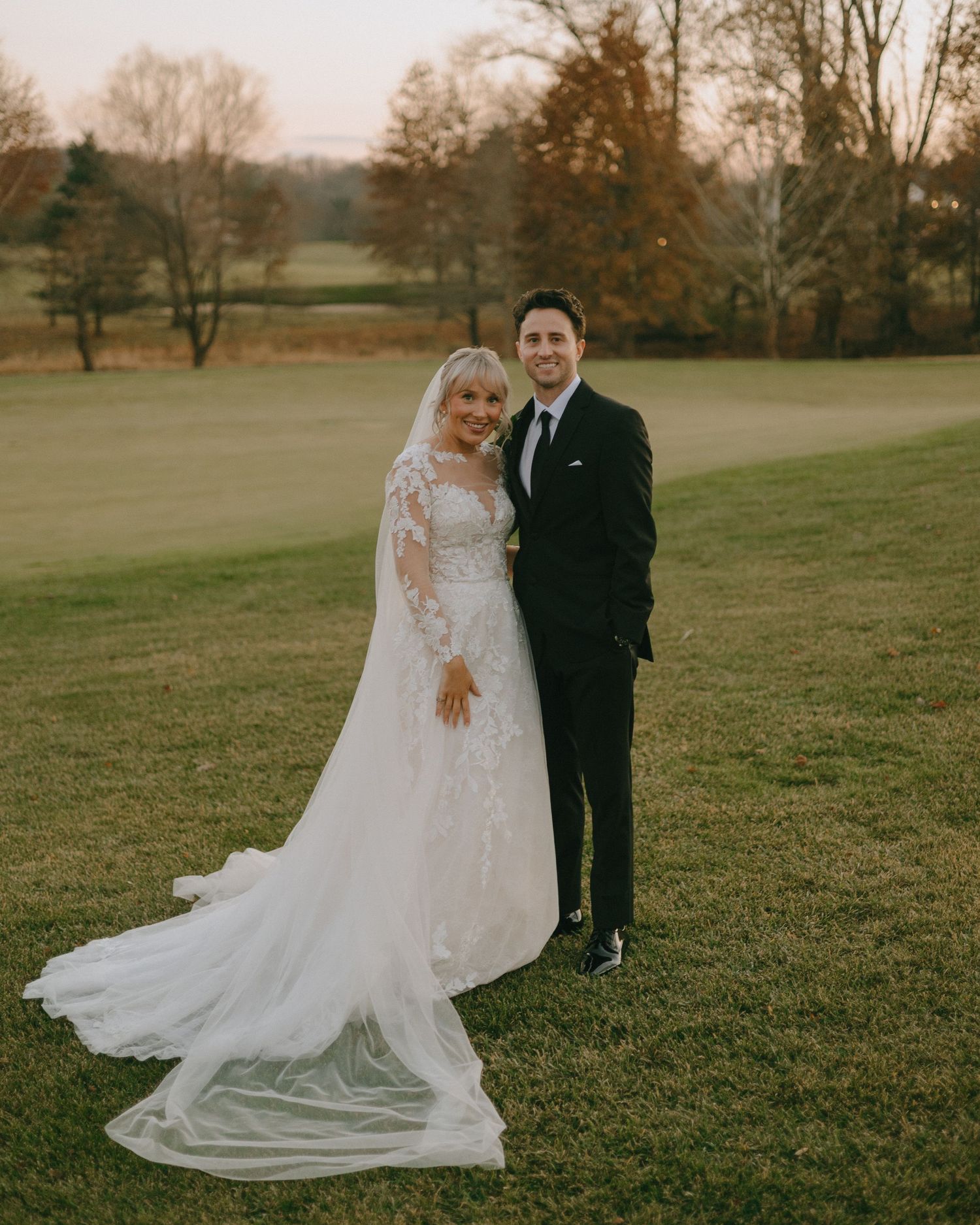 A couple takes wedding photos in a grassy field during golden hour.
