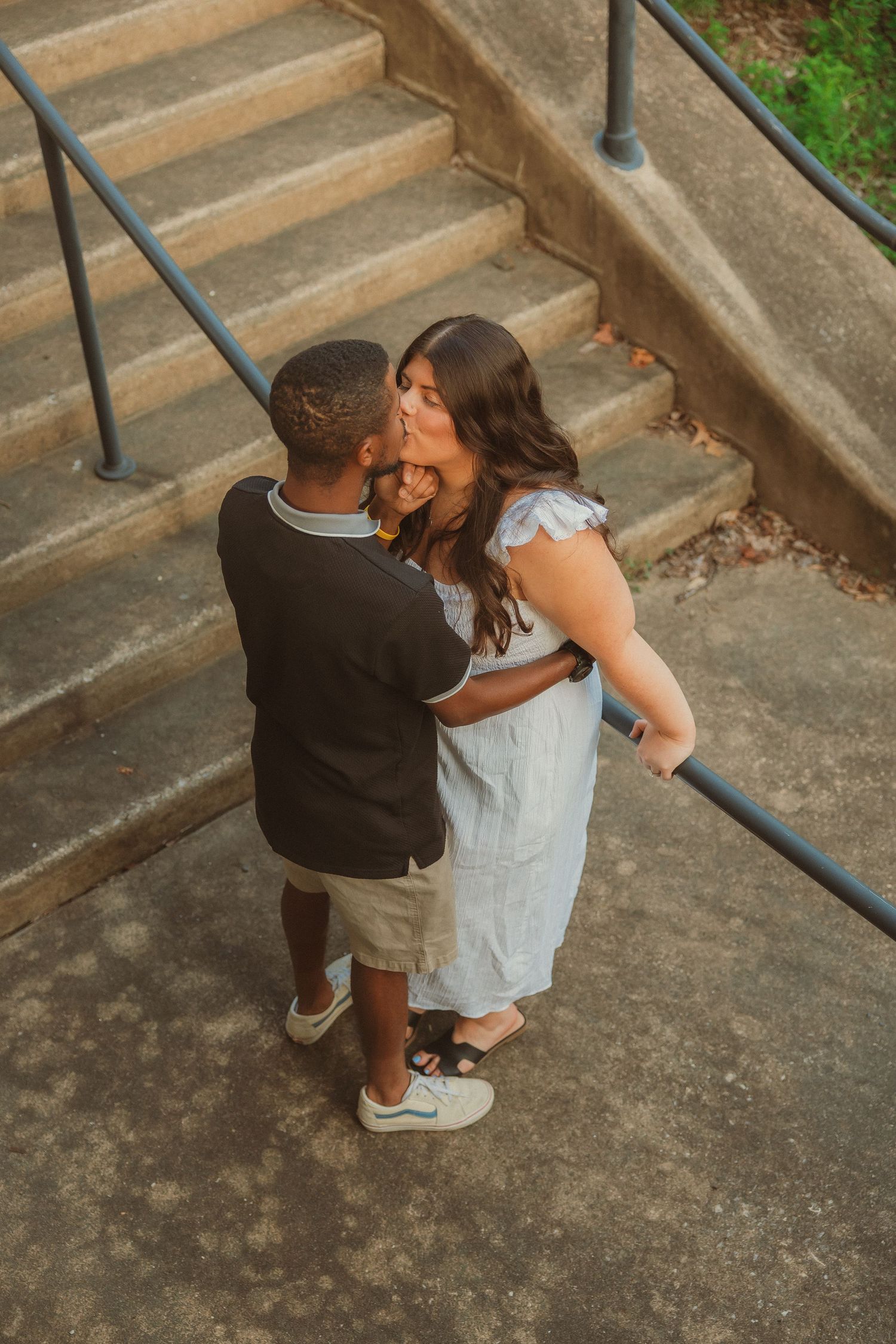 A couple shares an intimate moment on concrete steps outdoors.