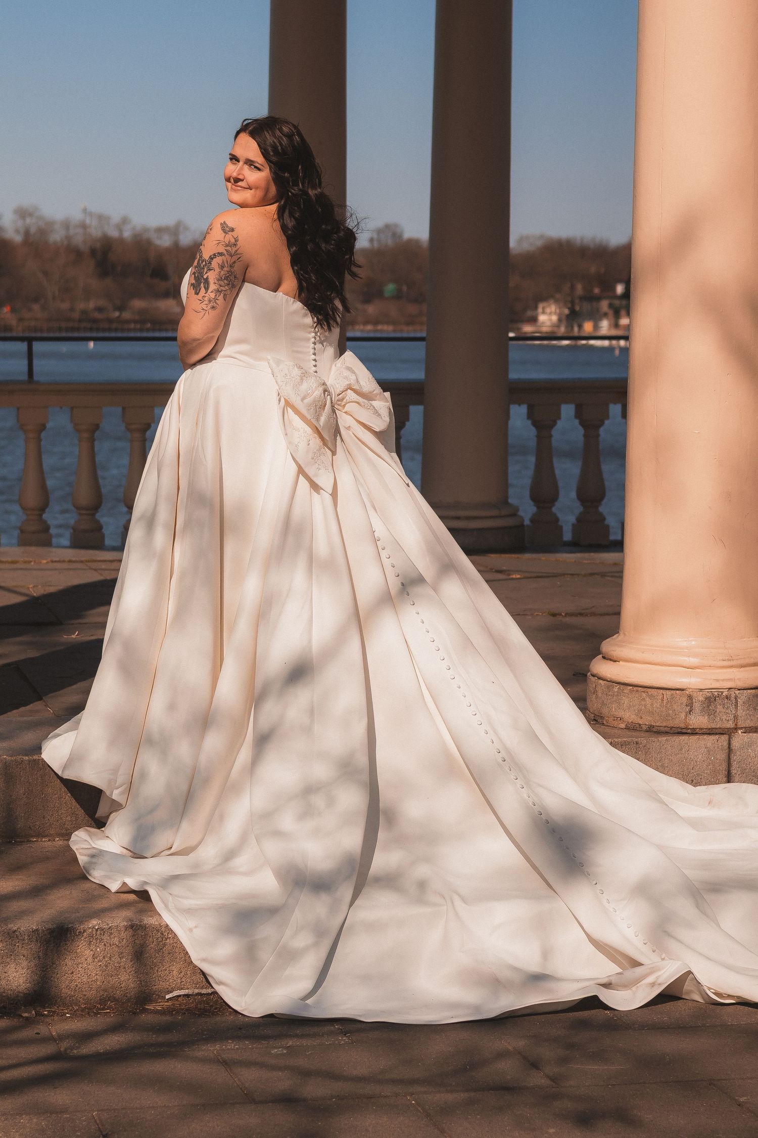 White wedding dress with flowing train elegantly draped across stone columns at sunset.