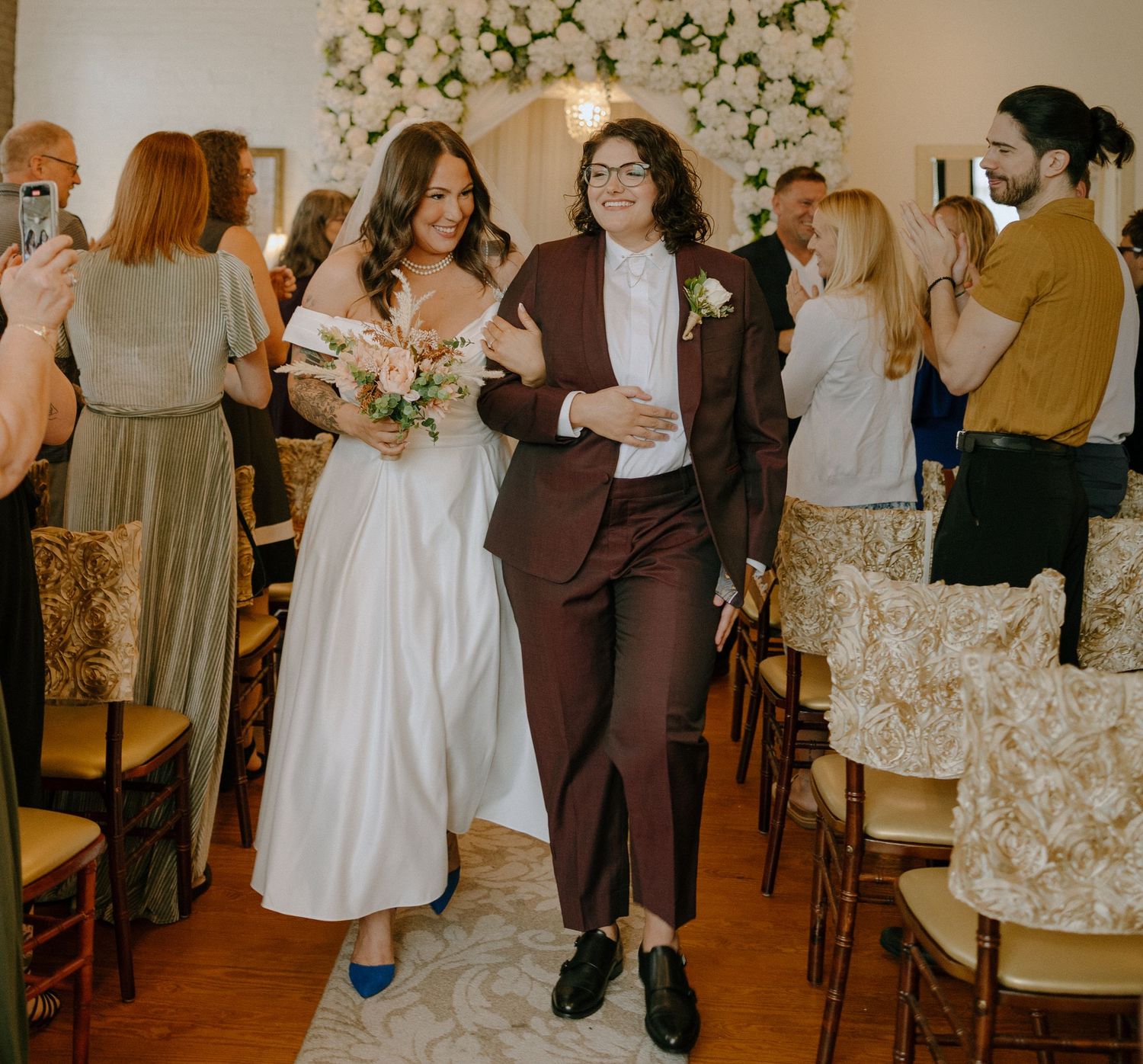 Wedding reception guests mingle and celebrate in an elegant venue decorated with floral arrangements and warm lighting.