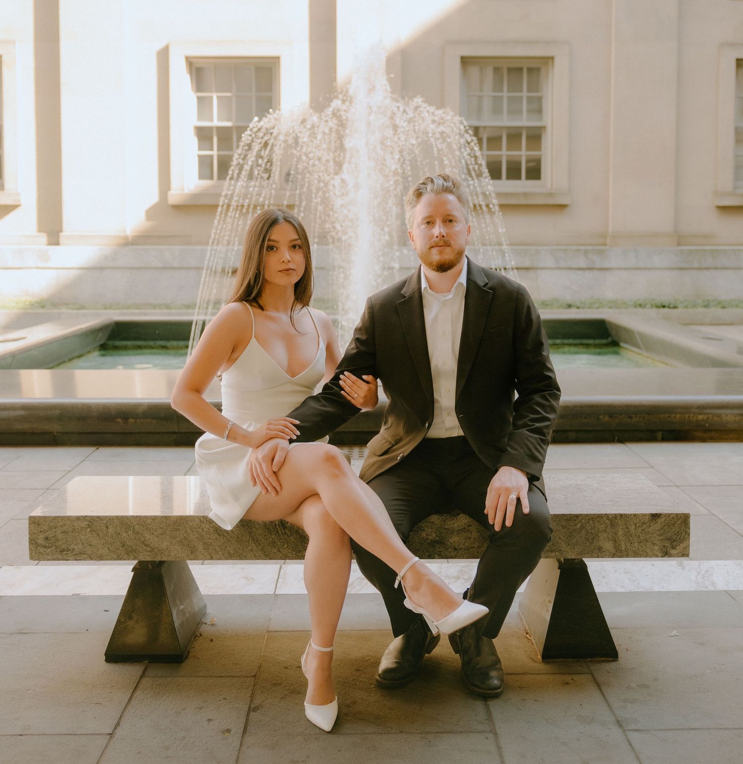 Stylish couple in formal attire sitting and dancing on stone steps.
