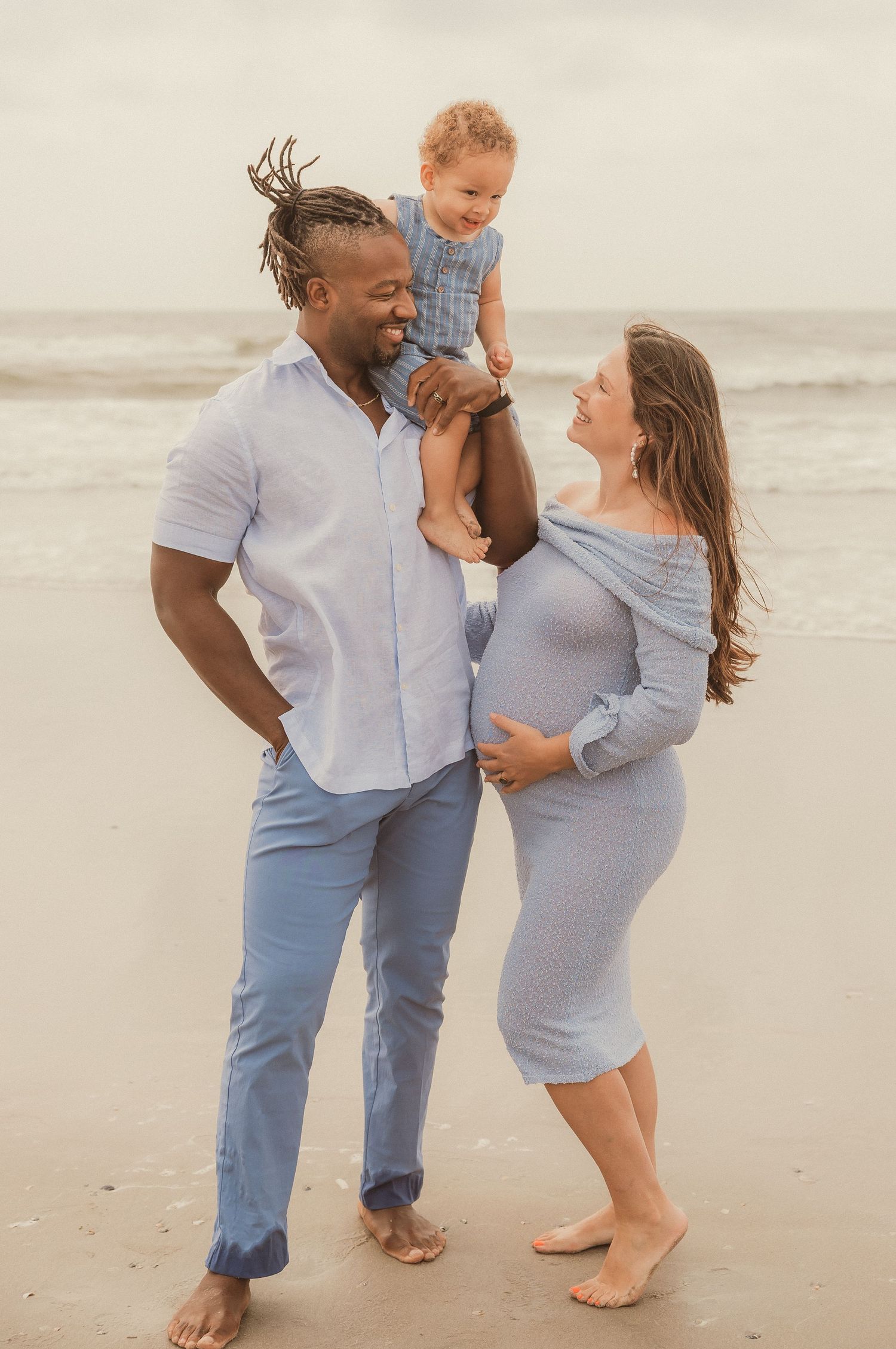Family in coordinating blue and white outfits sharing intimate moments on a cloudy beach.