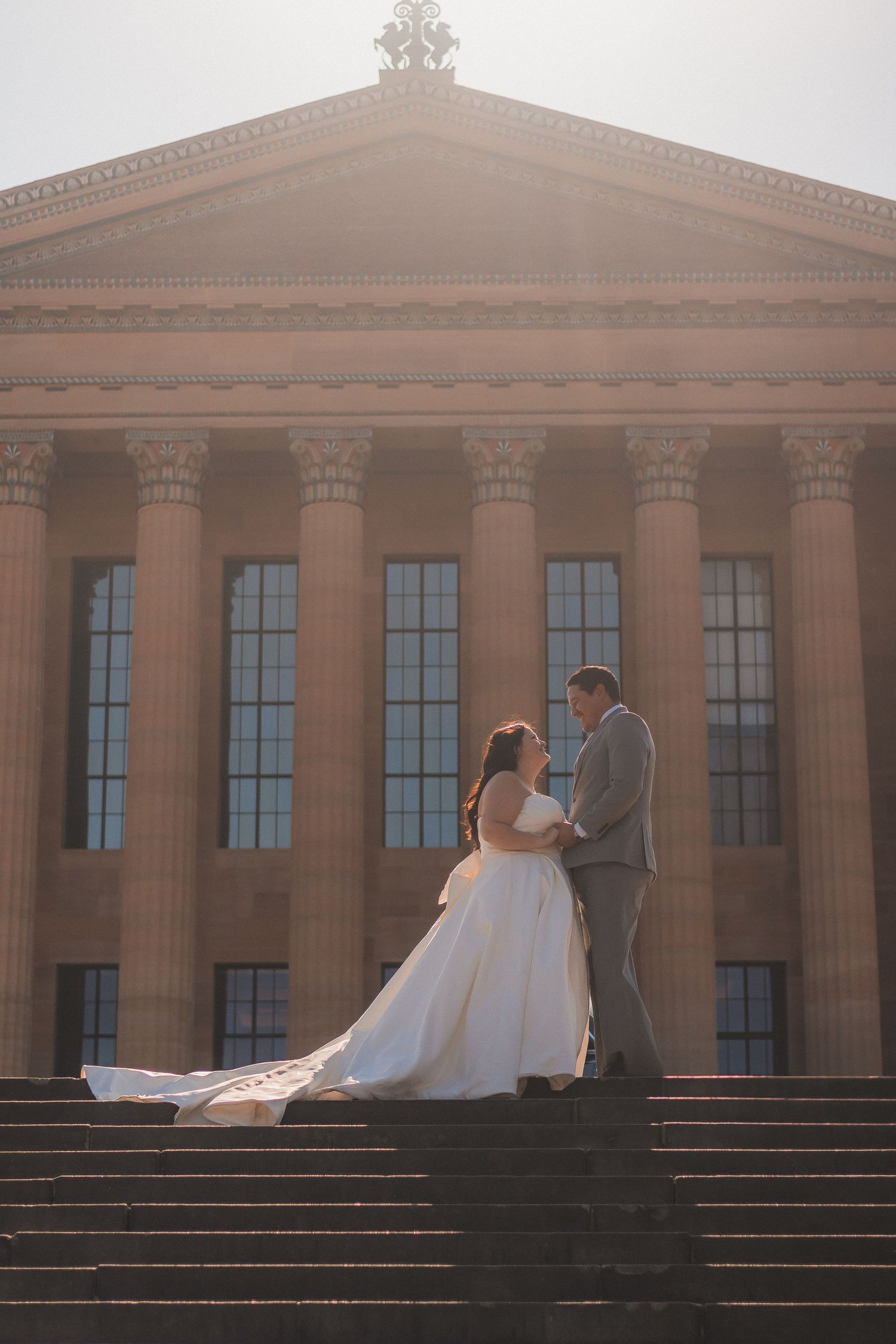 Wedding couple posing on grand stone steps of a neoclassical building with columns.