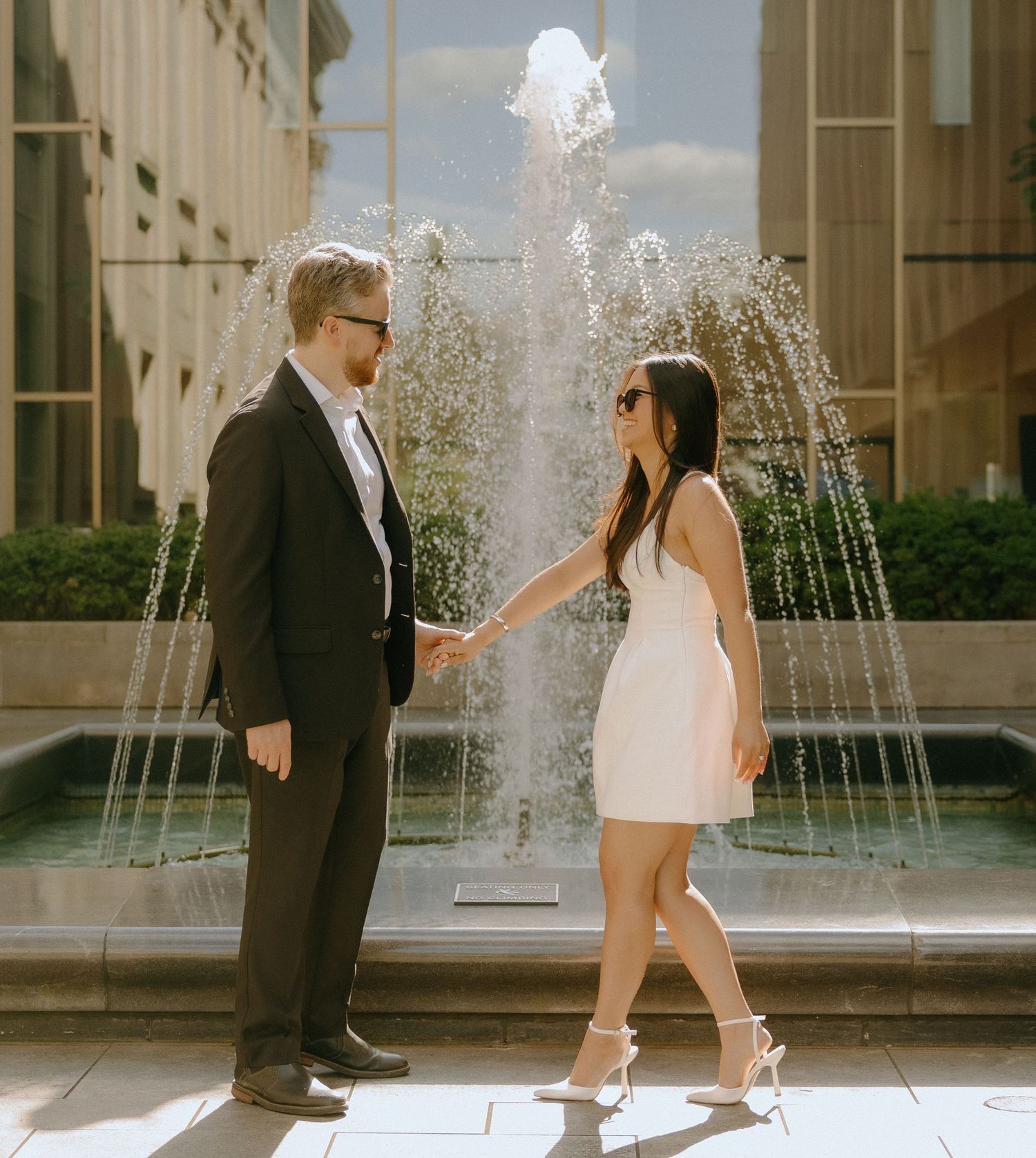 Dancing couple in contrasting black suit and white dress perform elegant steps near fountain.