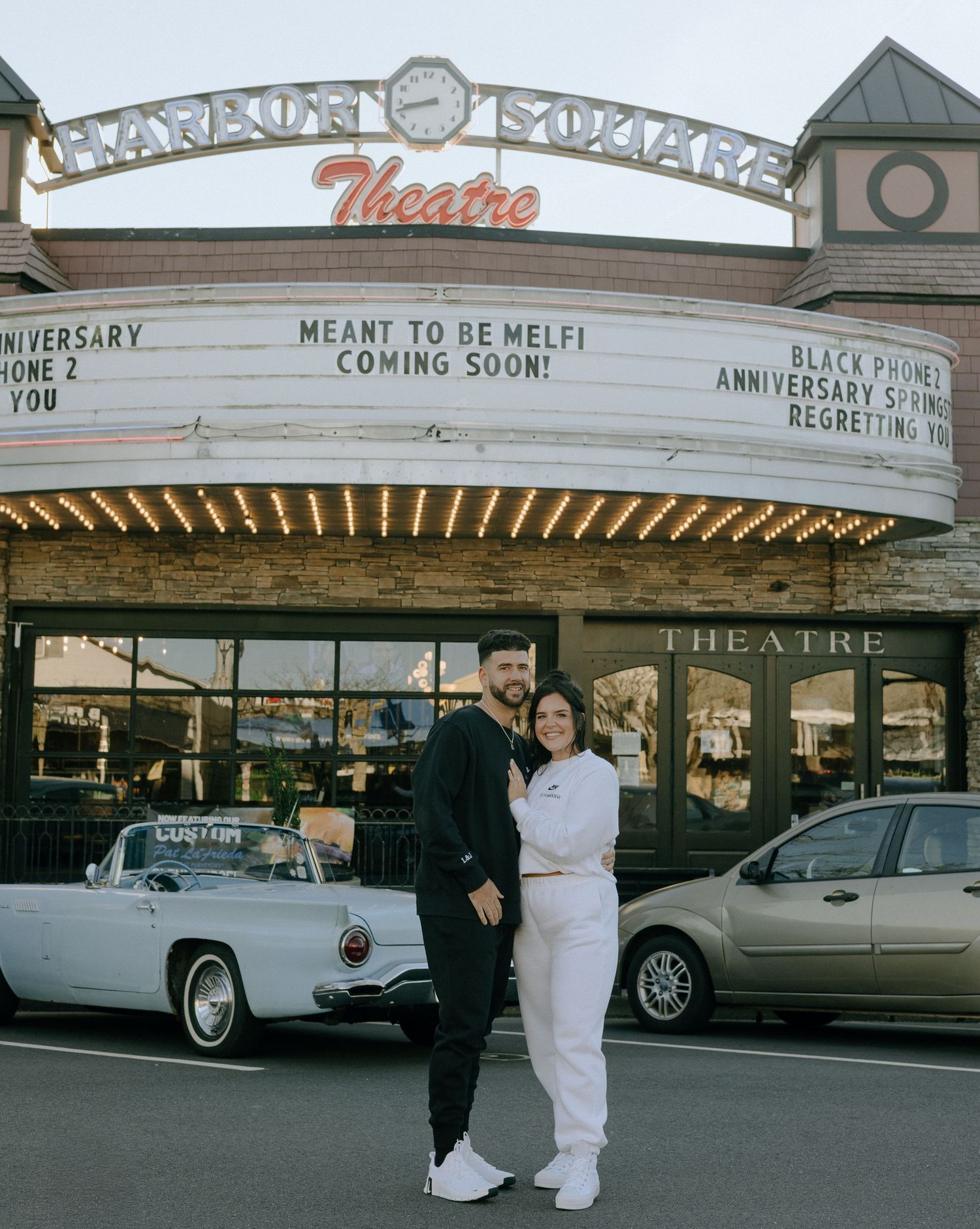 Classic cars parked outside a vintage movie theater with illuminated marquee signs.