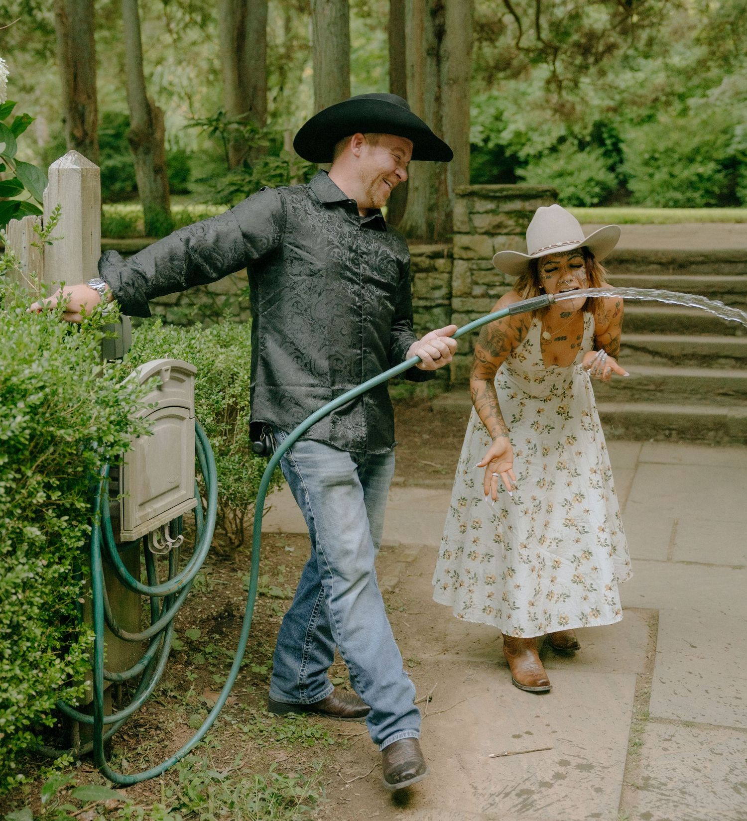 Couple in western attire plays and dances together near garden path.