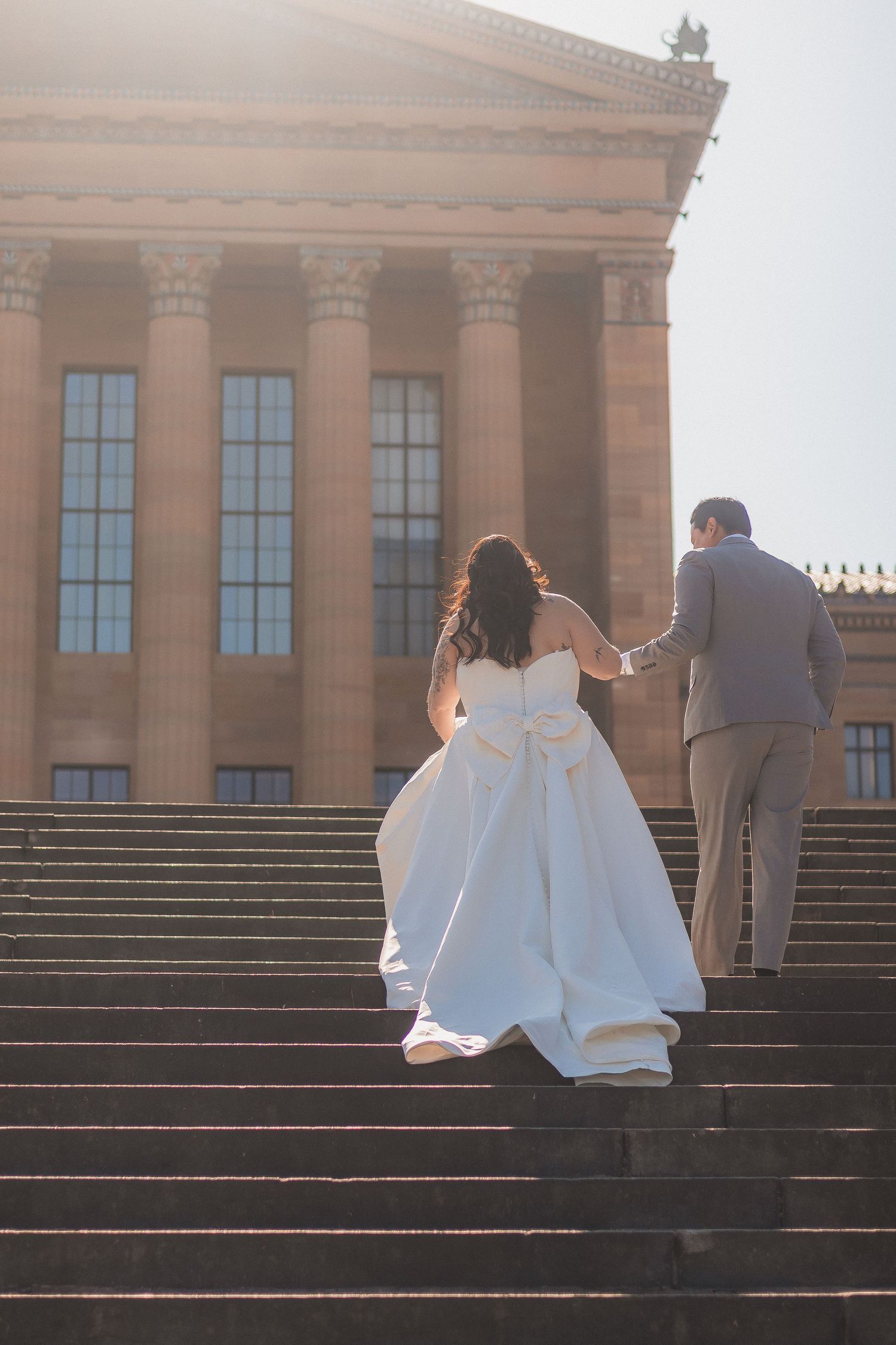 Couple in wedding attire sitting on grand stone steps in front of a historic building.