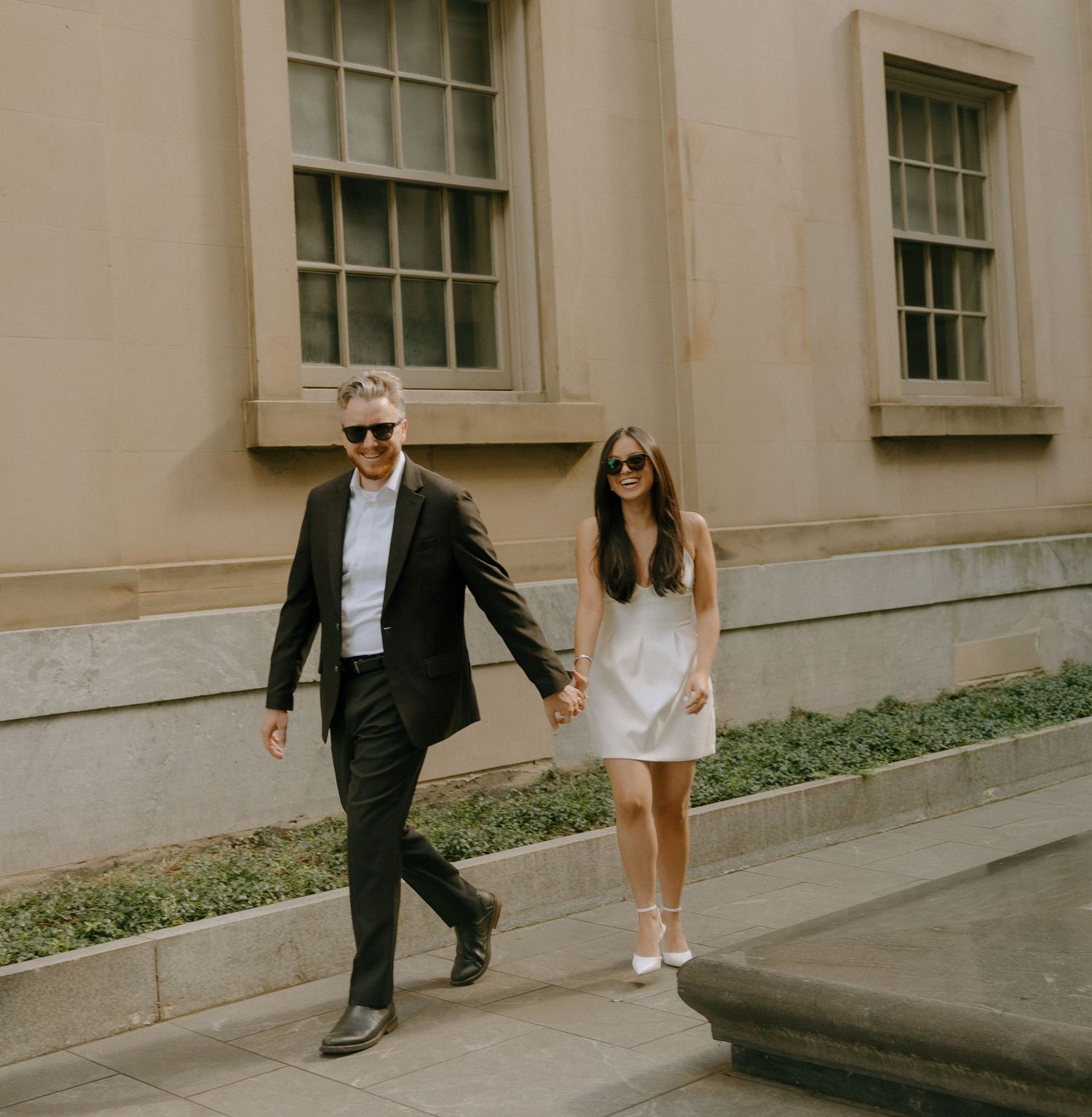 Stylish couple walking along a stone building exterior.