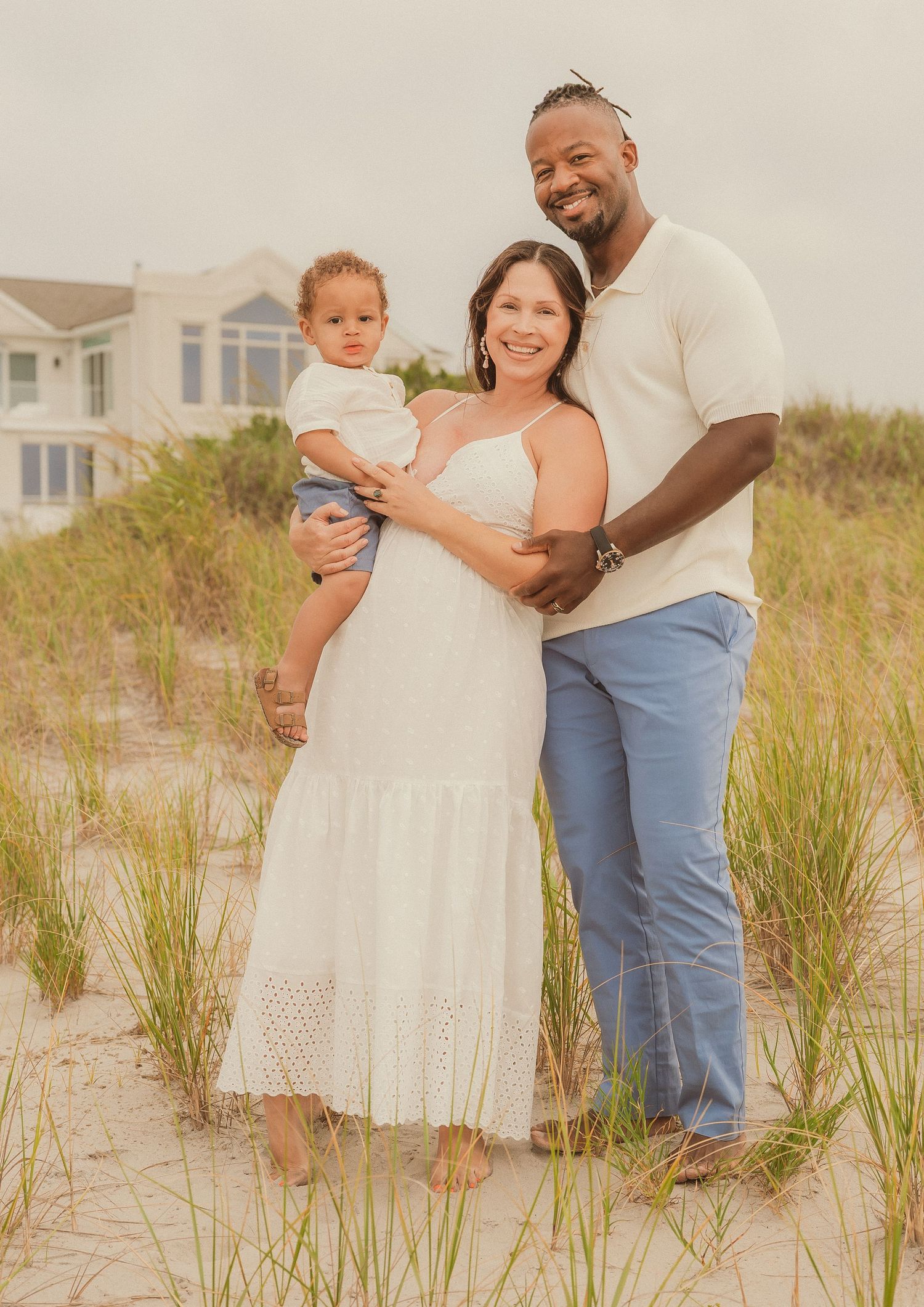 Candid family portrait taken at sunset on a sandy beach with beach houses in the background.