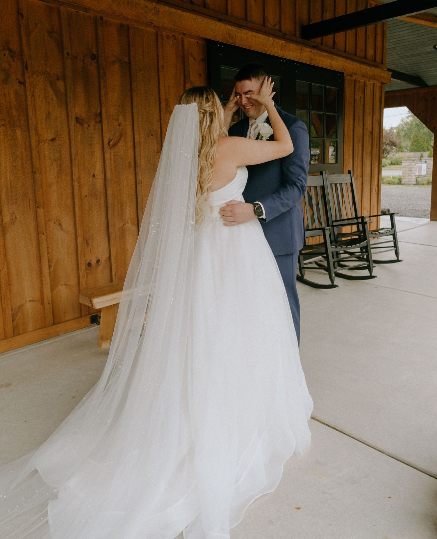 A couple in wedding attire dances together on a rustic wooden porch with rocking chairs in the background.