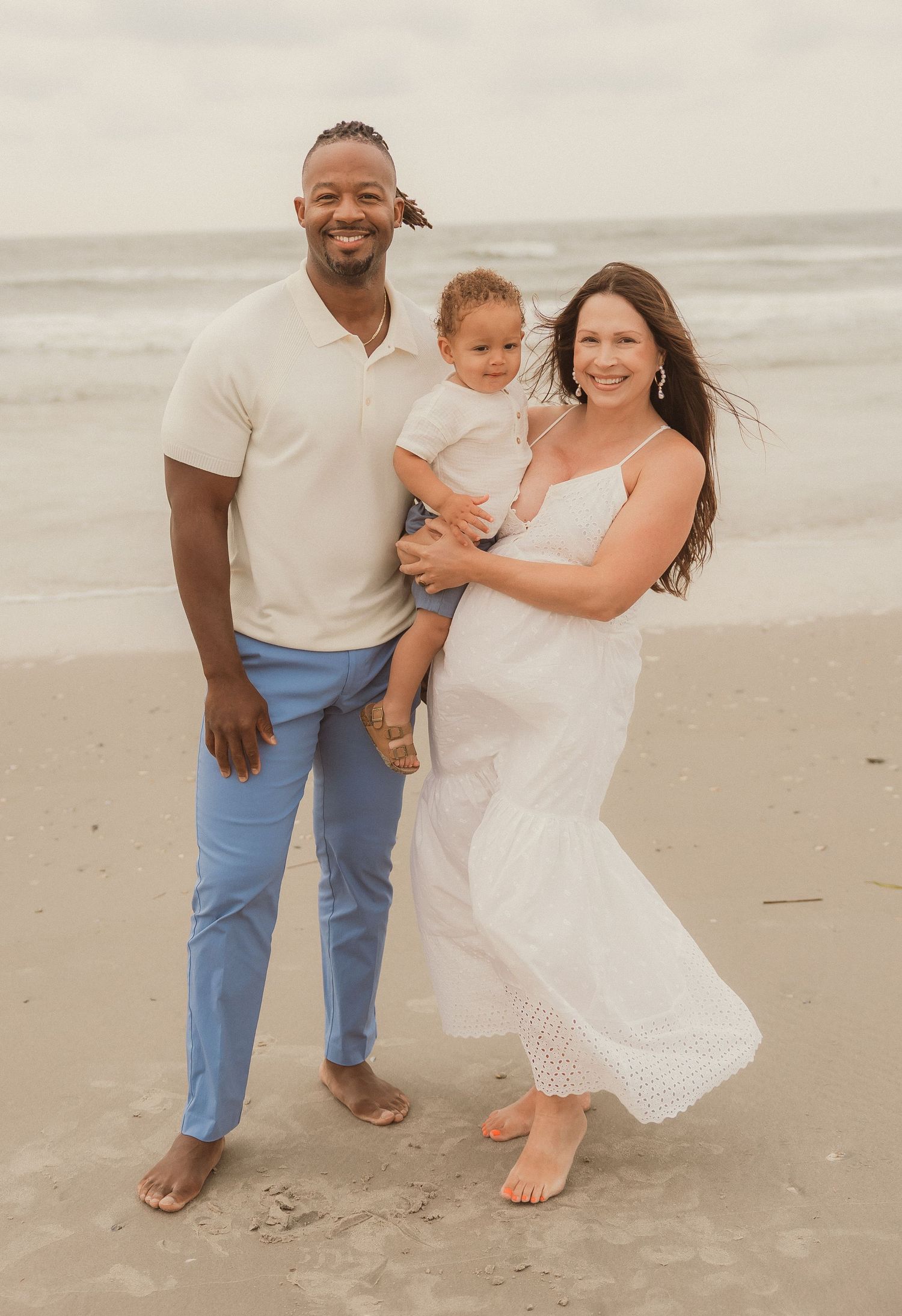 Family wearing coordinated outfits poses casually on beach during sunset.