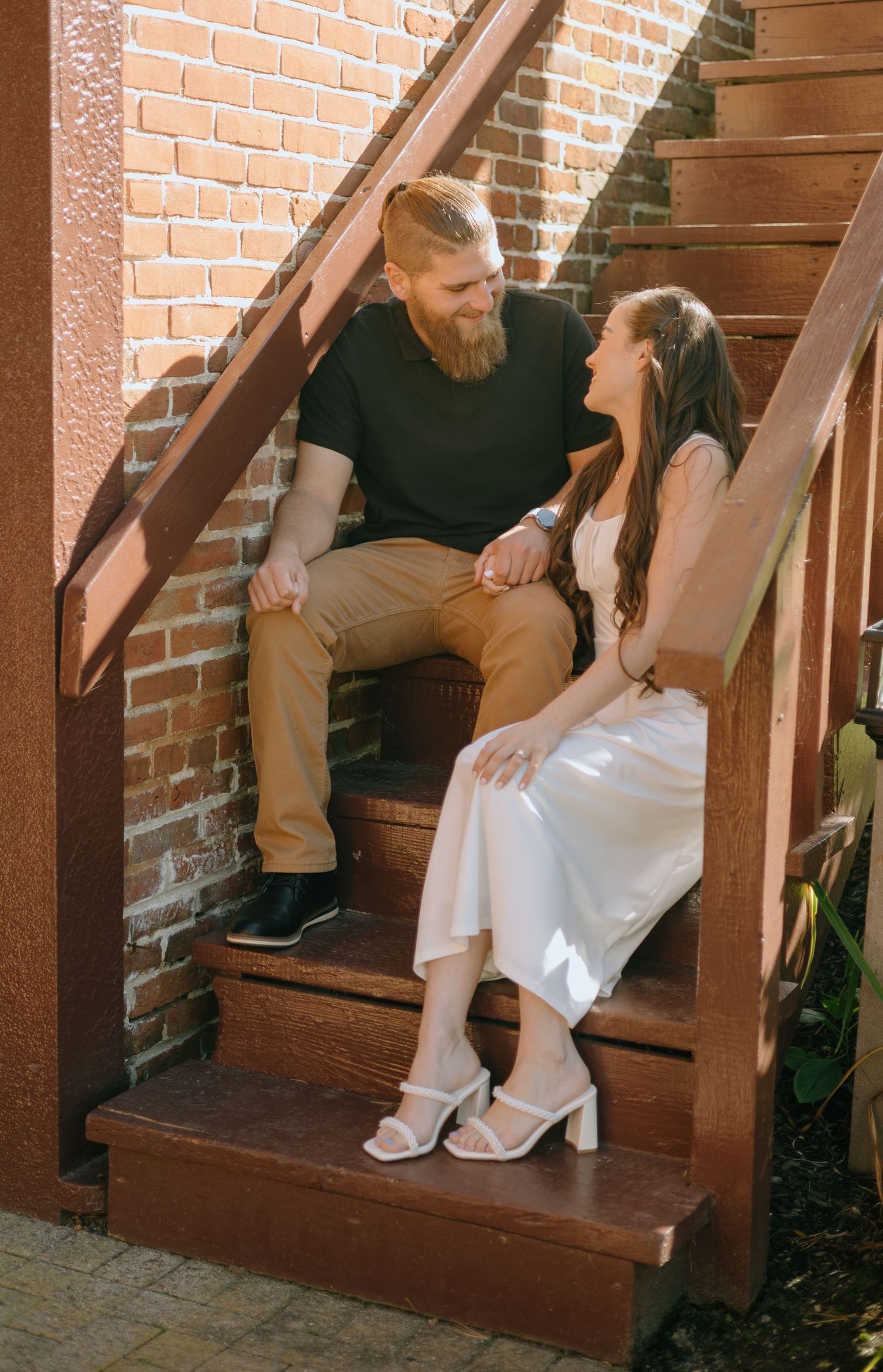 Two people sitting on wooden stairs against a brick wall in warm lighting.
