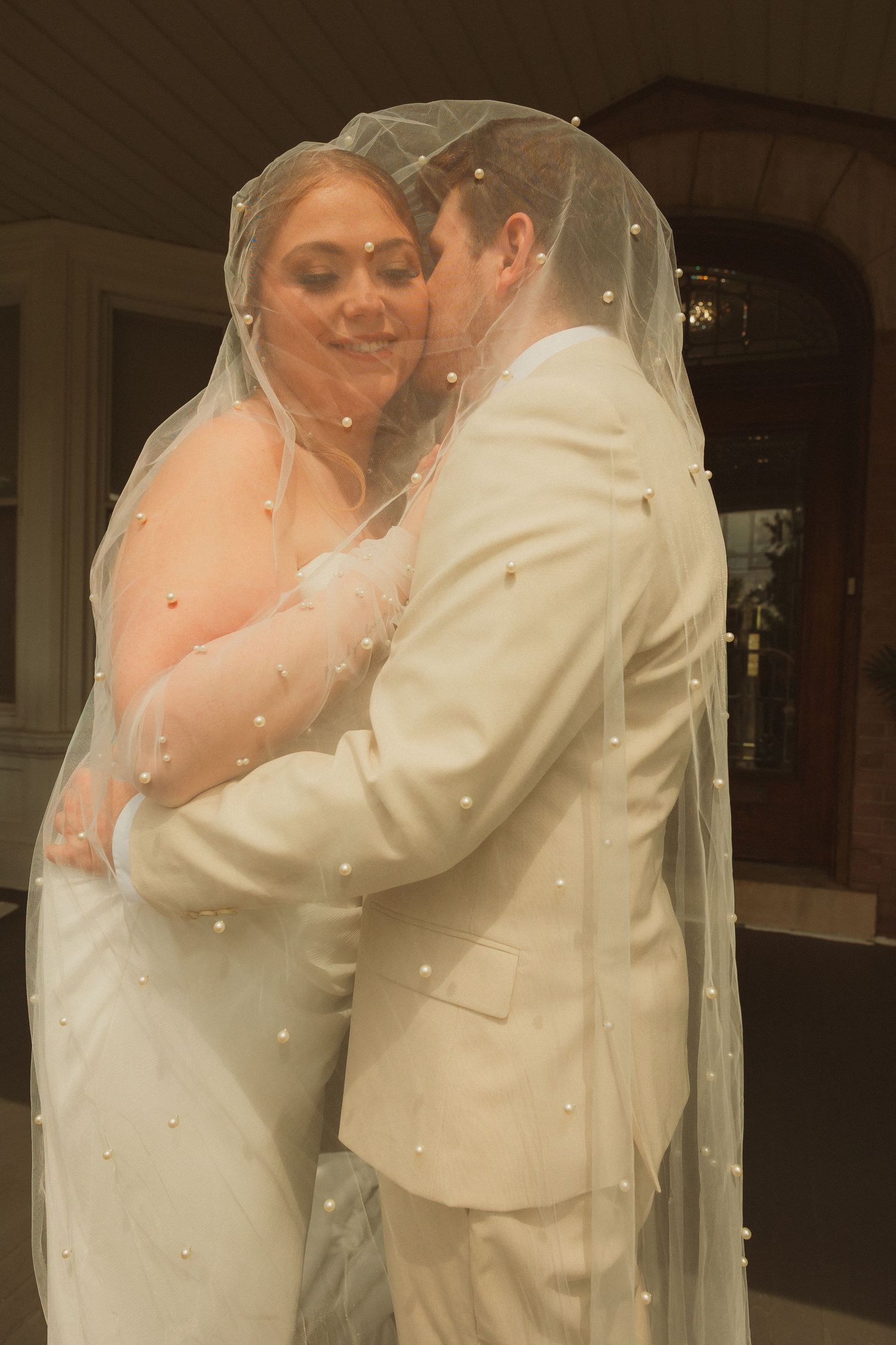 Romantic wedding couple embrace under flowing white veil.