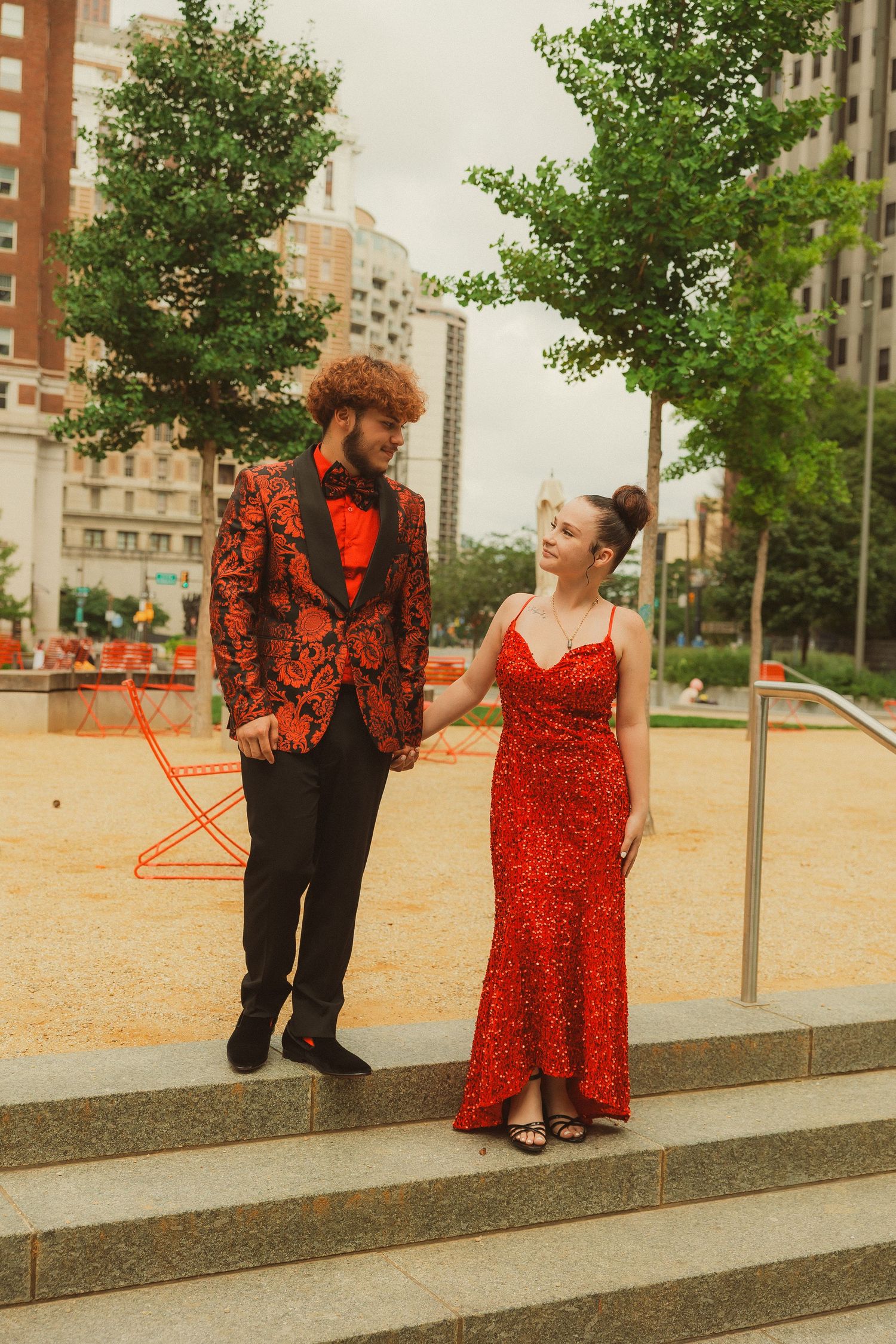 A couple poses on stone steps with red LOVE sculpture visible in the background.