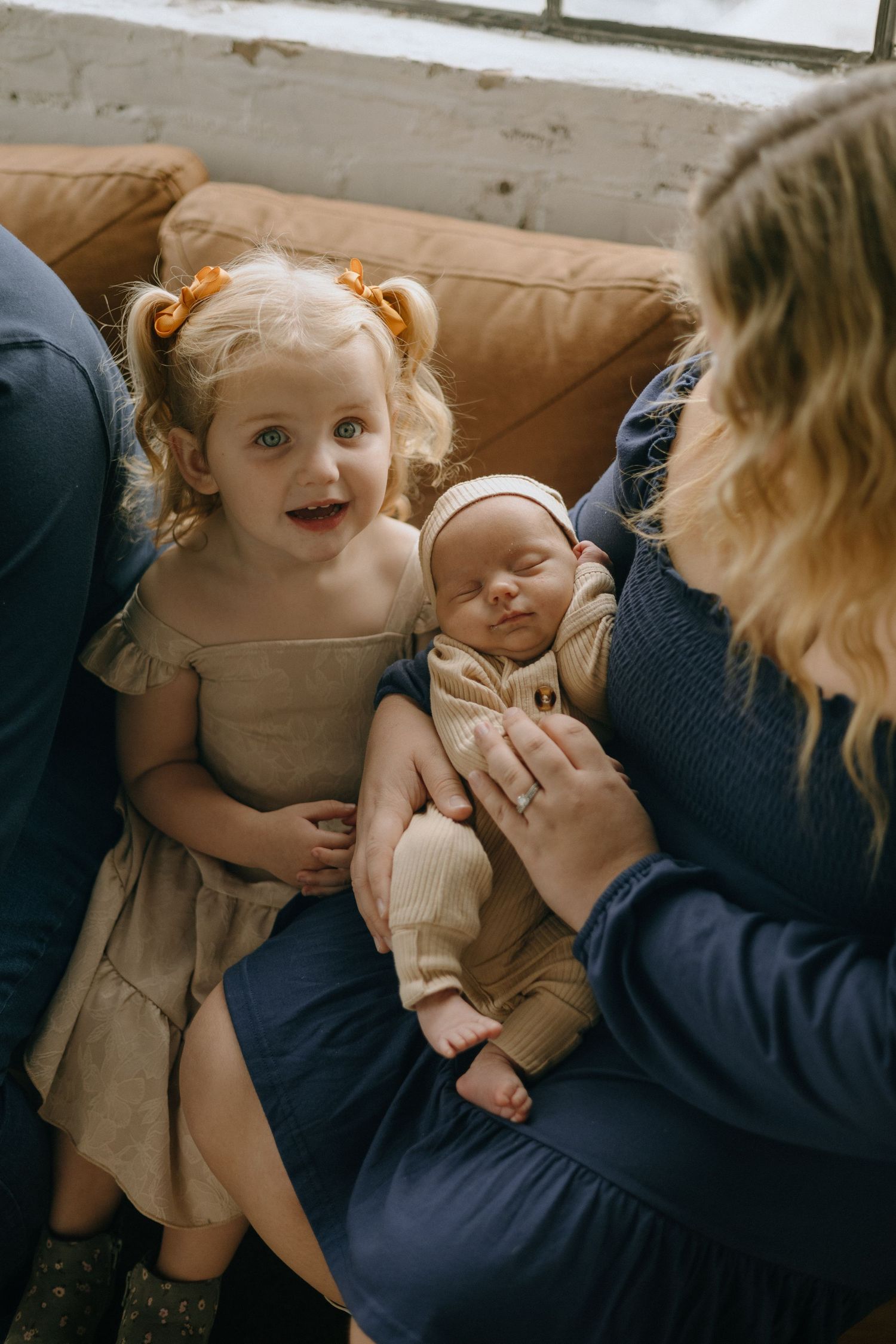 Lifestyle family photography showing intimate moments between siblings on a brown couch in natural light.