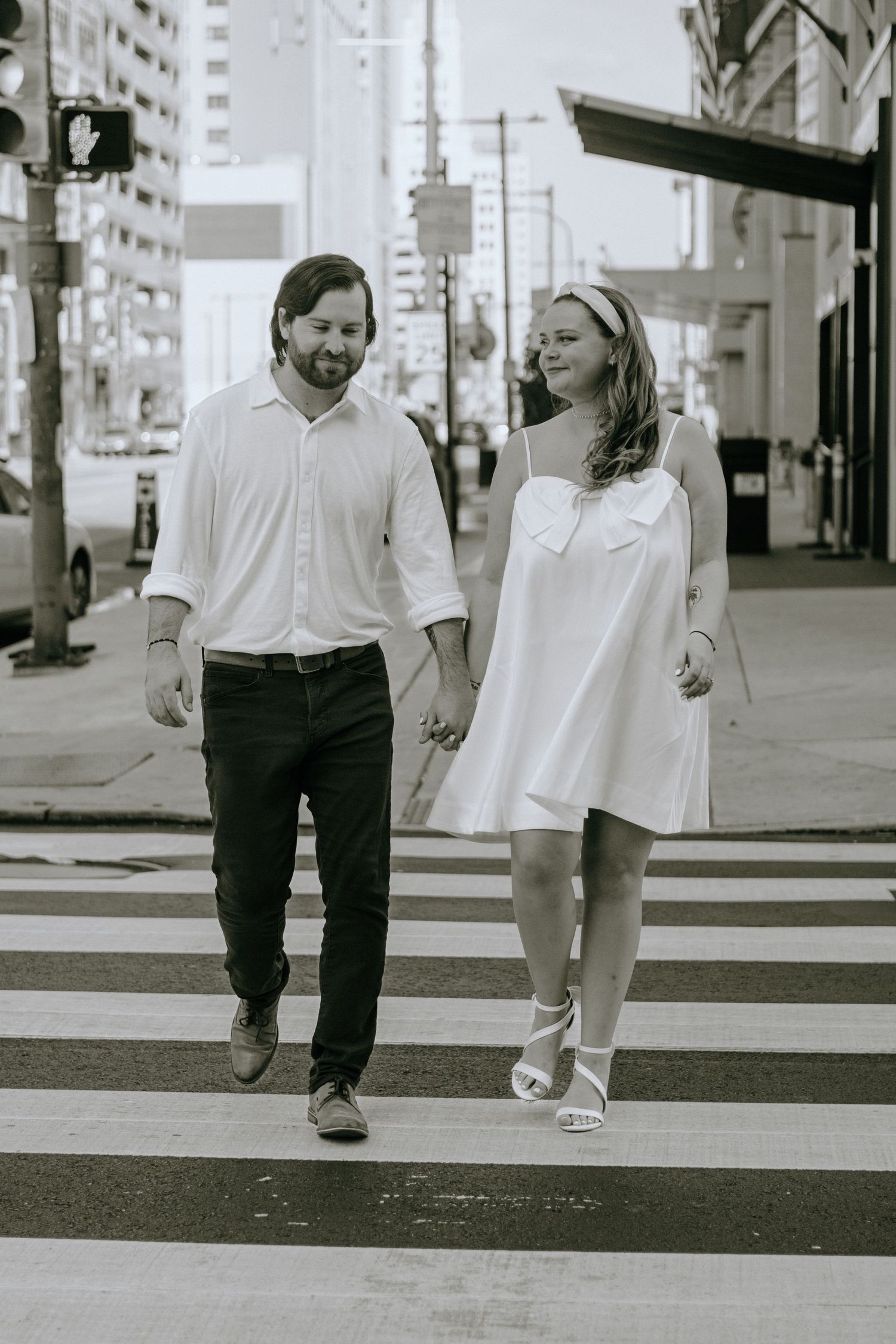 Black and white photo showing two pairs of legs walking together on a sidewalk, with one wearing pants and one in a dress.