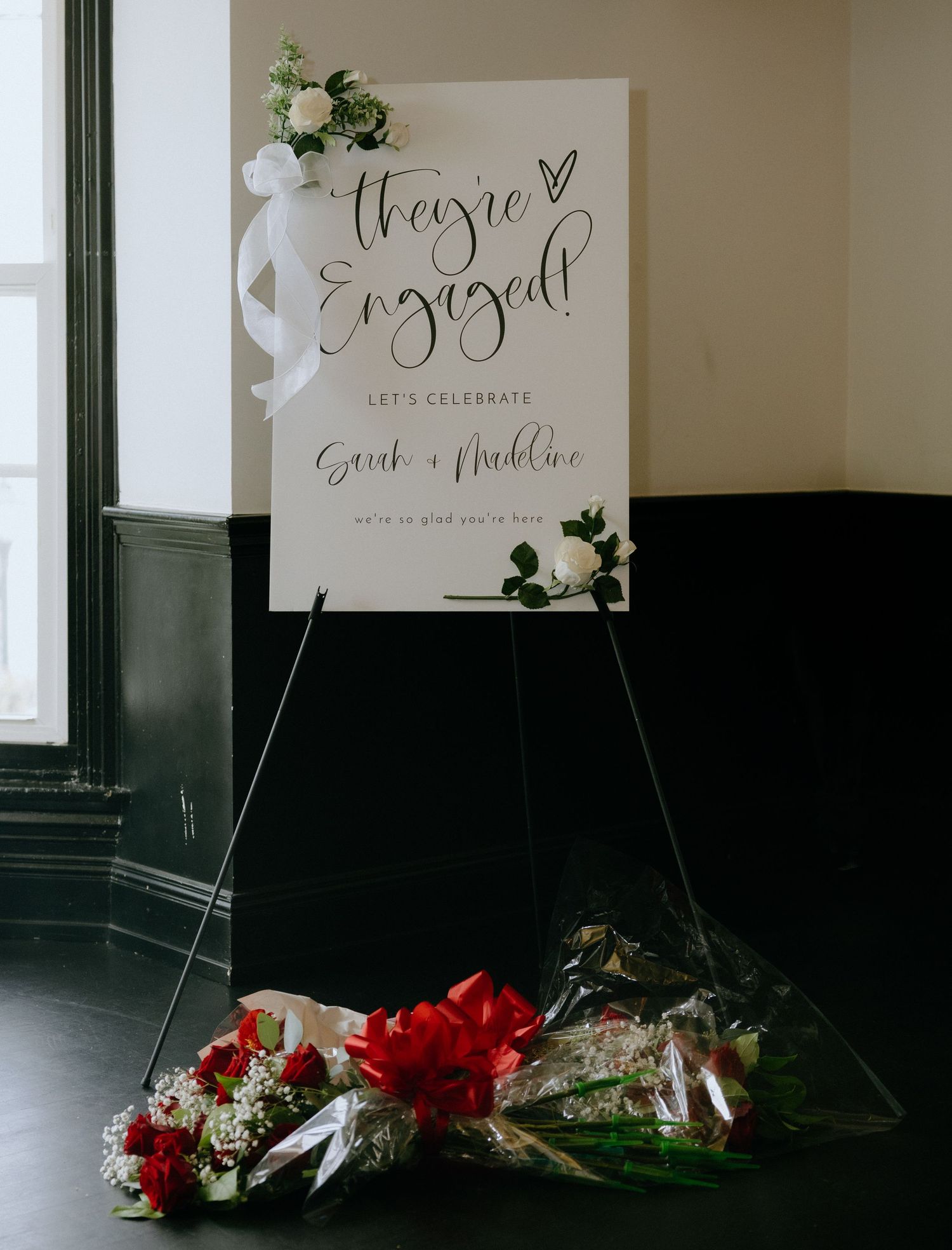An engagement celebration sign with floral decorations and red roses on a display stand.