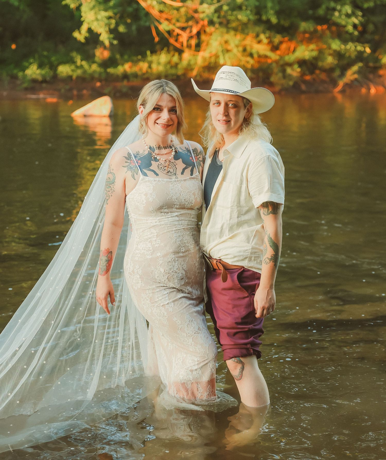 A happy couple standing in a river during their wedding photoshoot.
