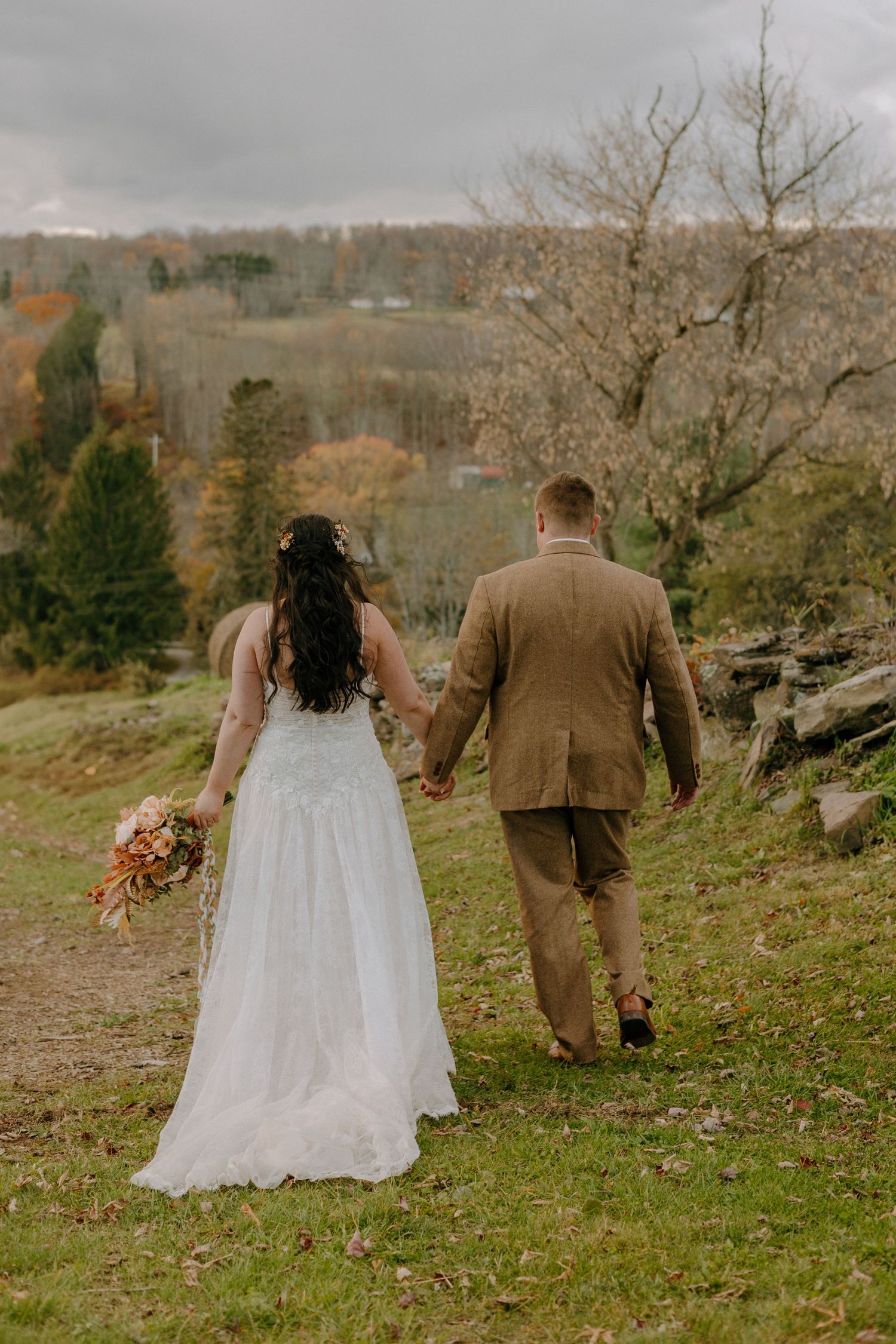 A couple walks hand in hand across a scenic hillside during their autumn wedding.