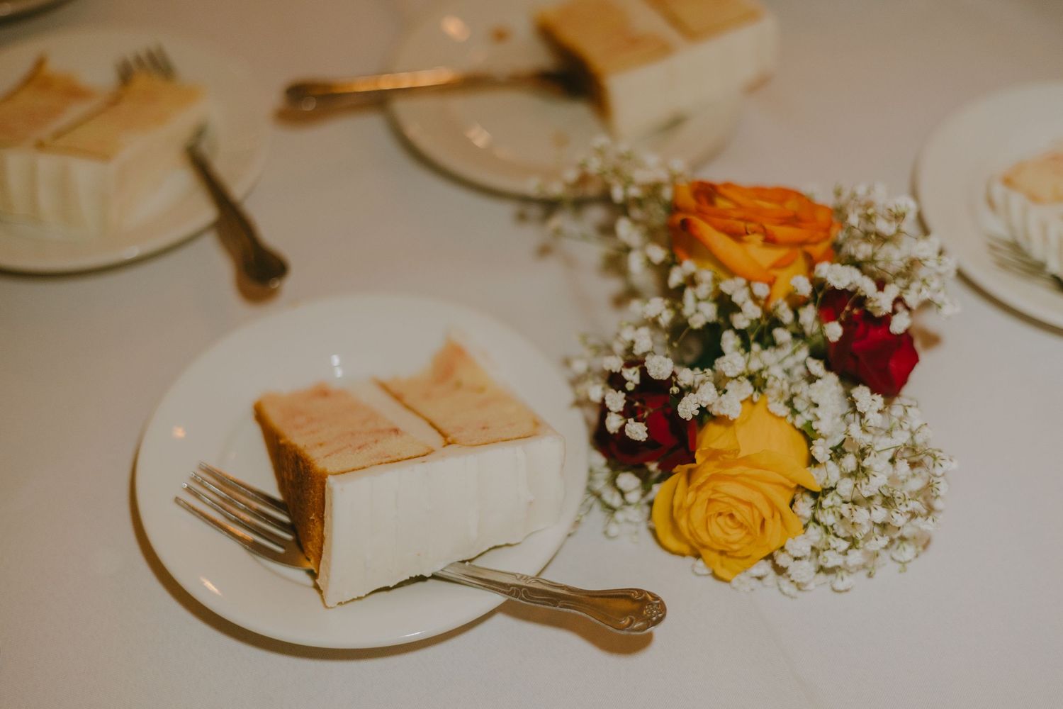Wedding table setting with white cake slices on plates and colorful roses with baby's breath centerpiece.