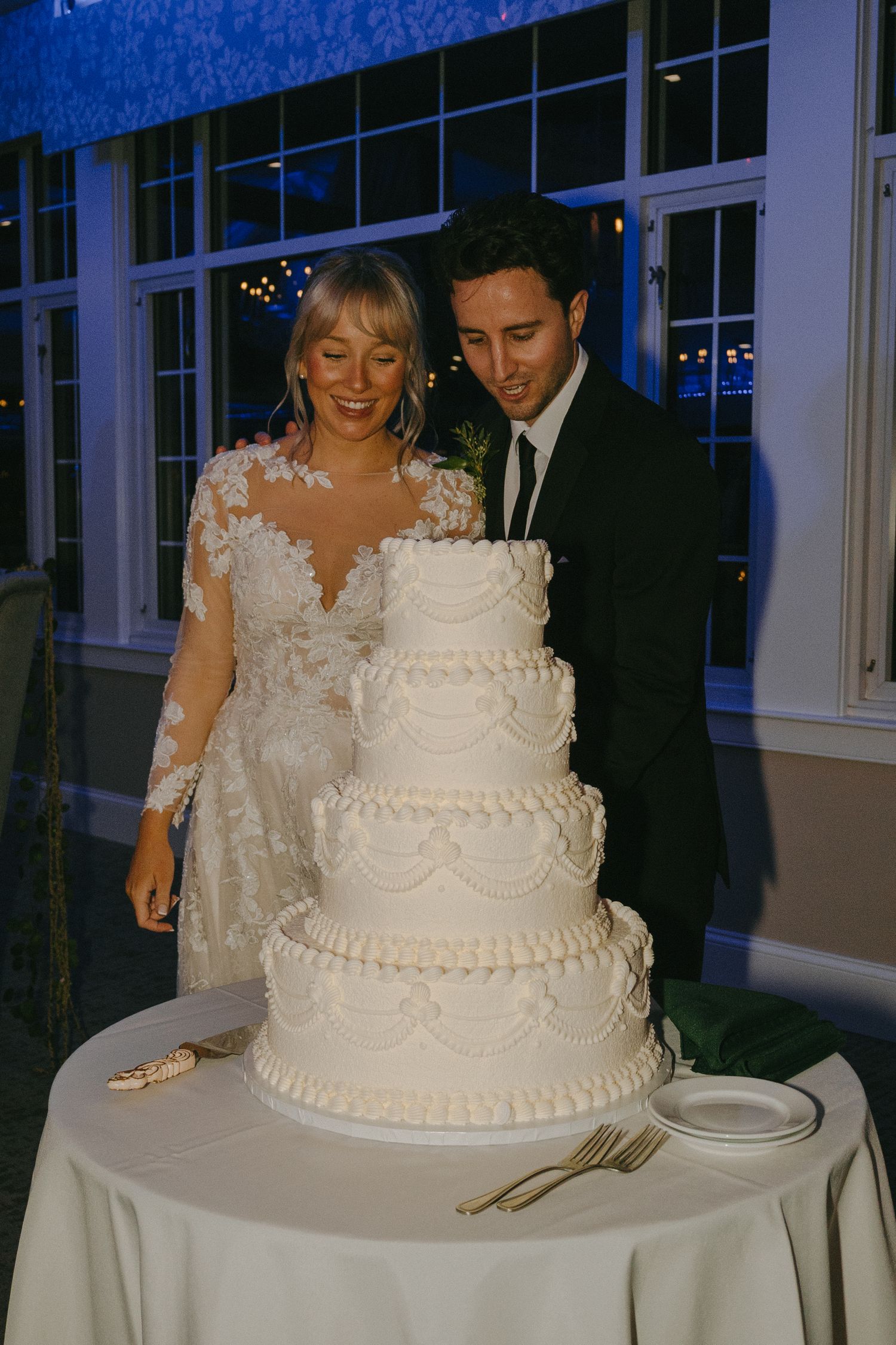A traditional white tiered wedding cake is displayed as newlyweds prepare to cut it at their reception.