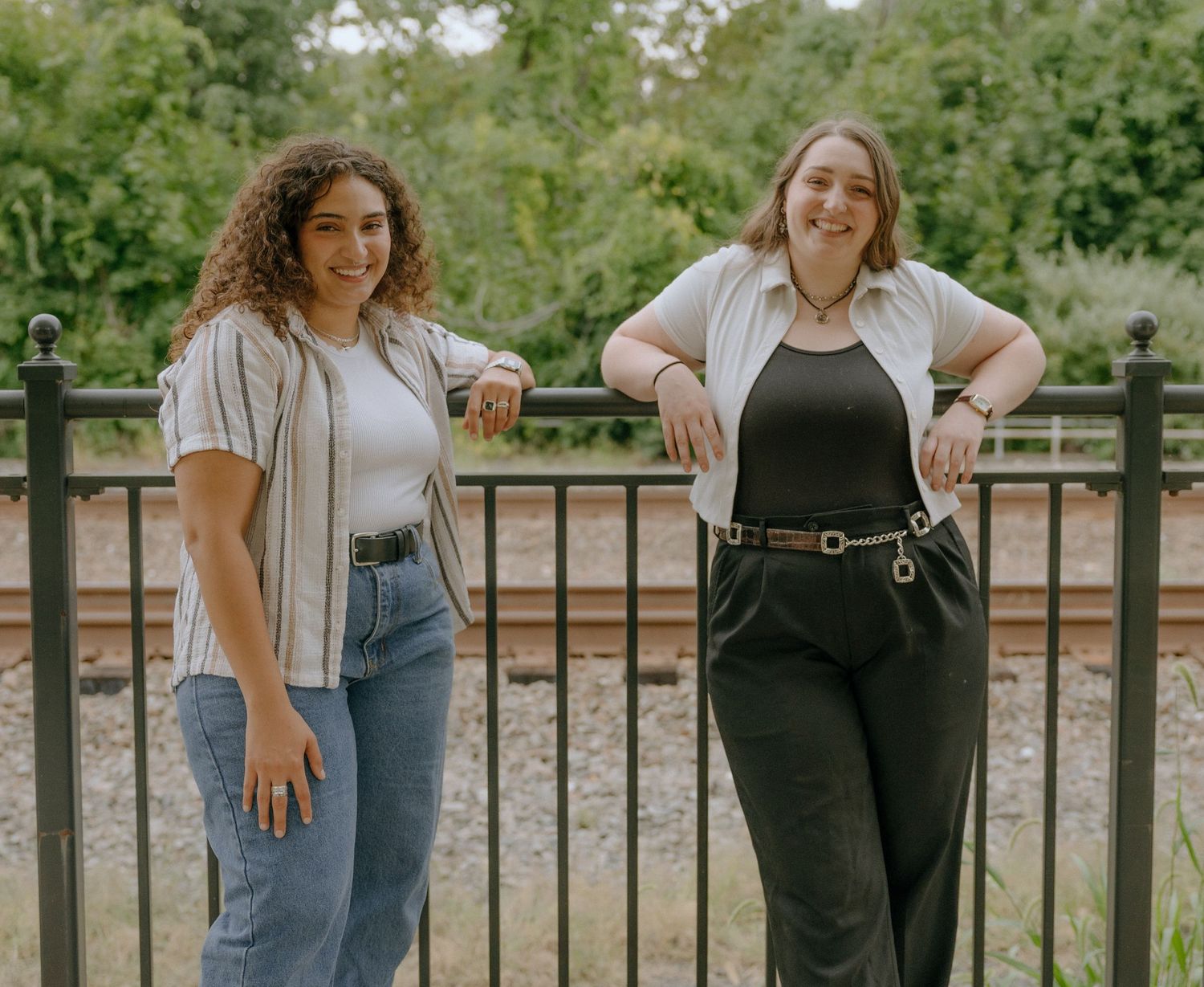Candid outdoor photoshoot poses along wooden railing in park setting.