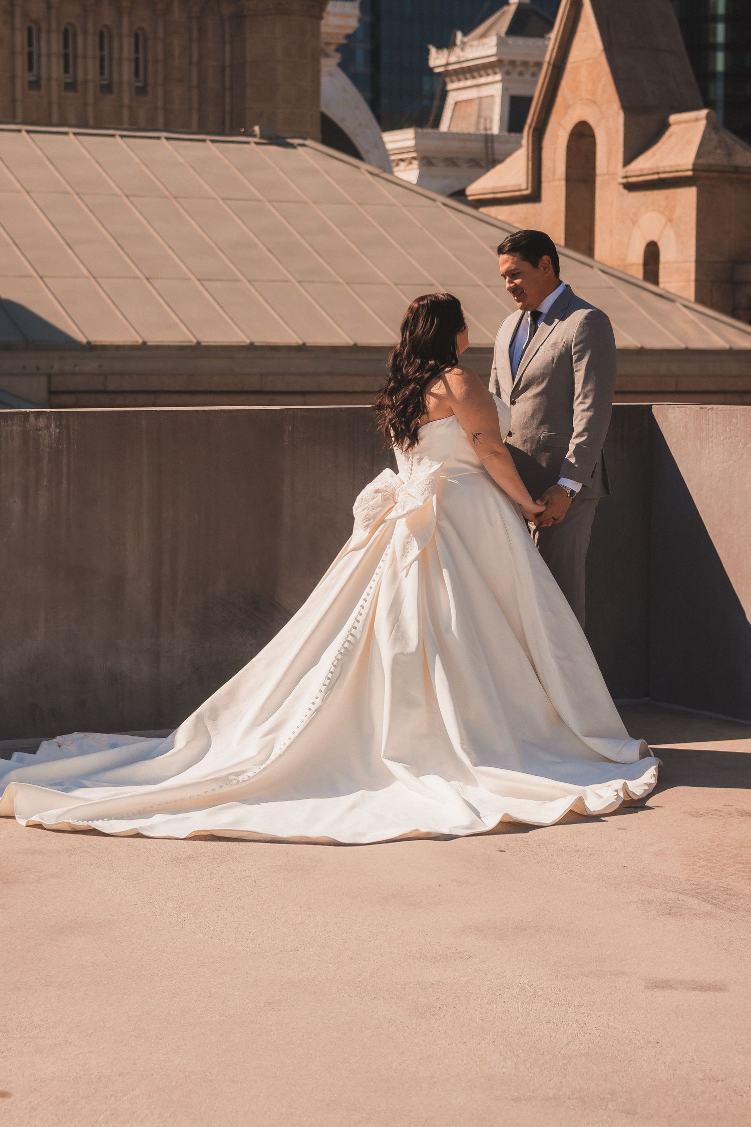 Elegant wedding portrait with bride's flowing dress against architectural backdrop.