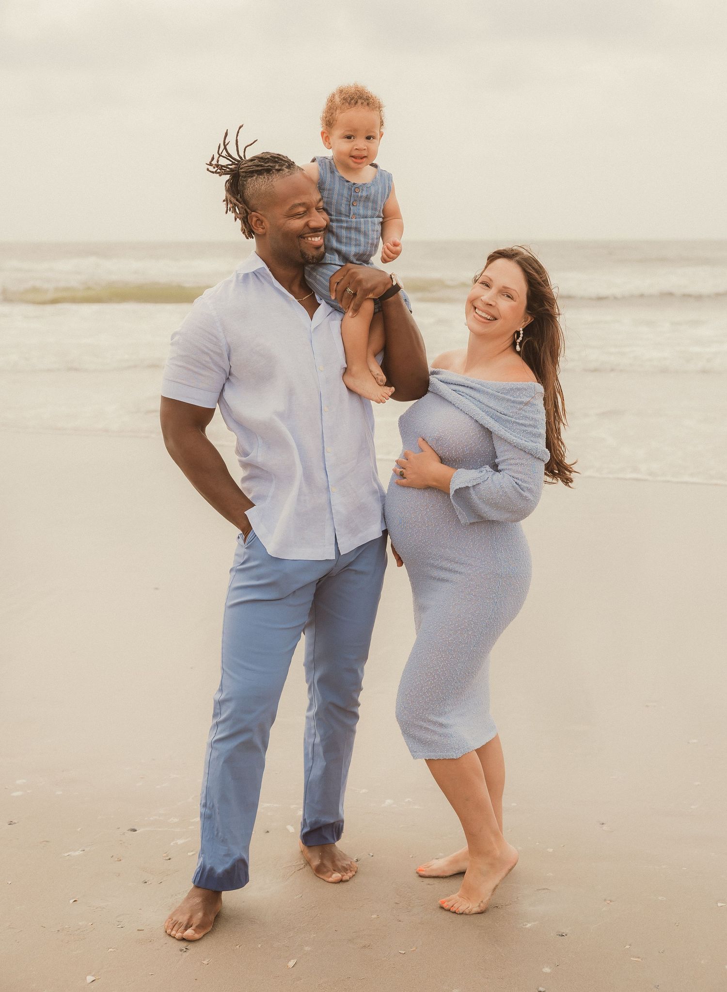 Family in coordinating blue and white outfits plays together on beach.