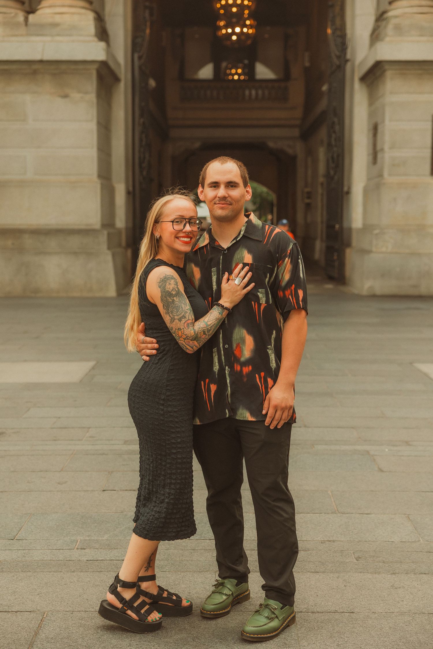 A couple poses together on a stone plaza in casual urban attire.