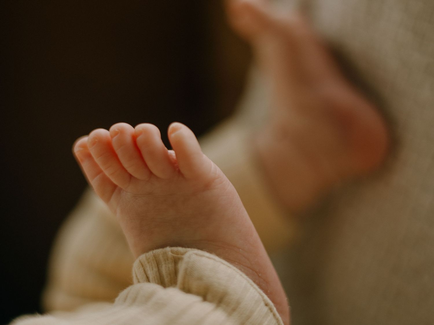 Close-up photo of tiny newborn baby feet with delicate pink toes against a dark background.