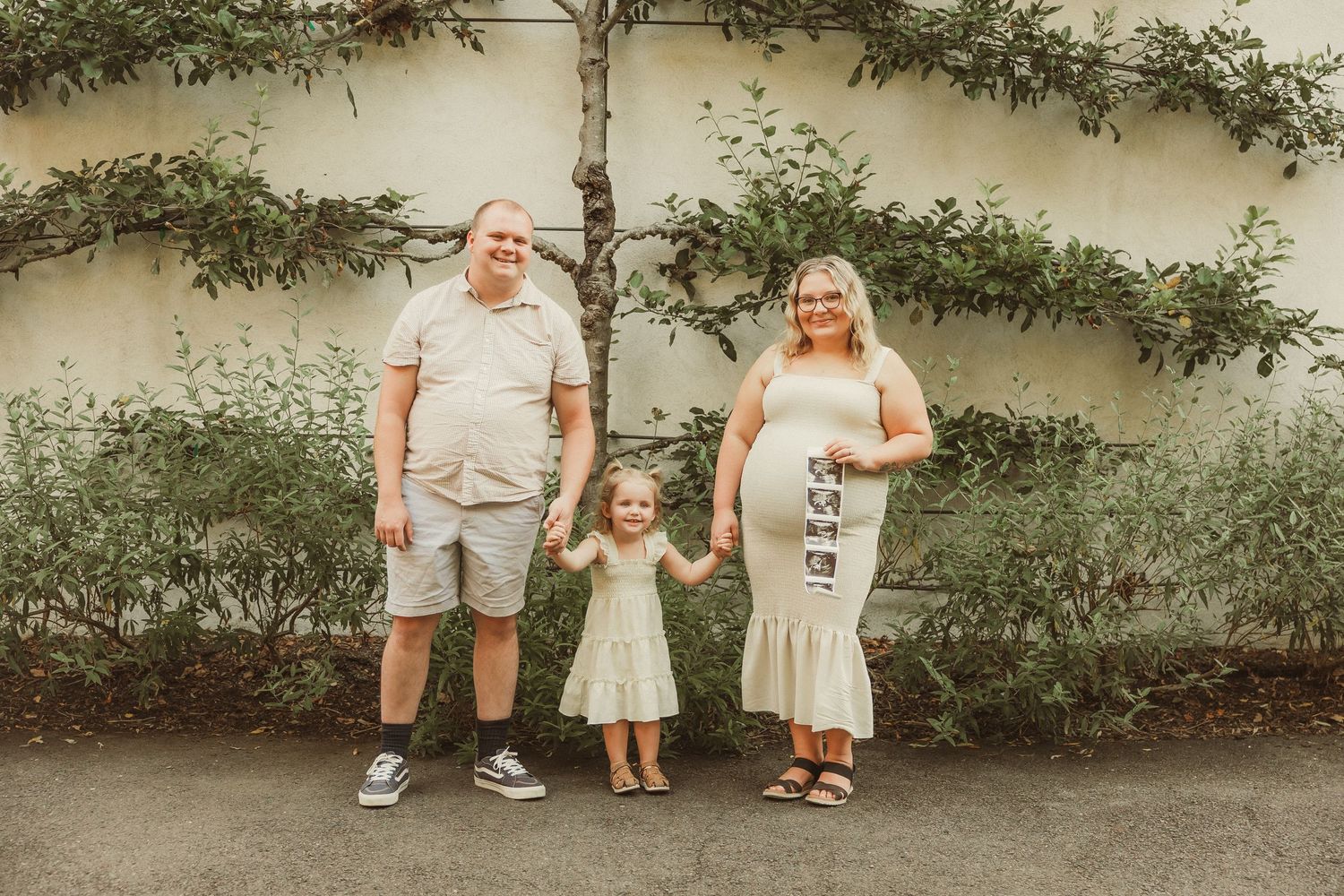 Family portrait series against cream wall with climbing vines and greenery.
