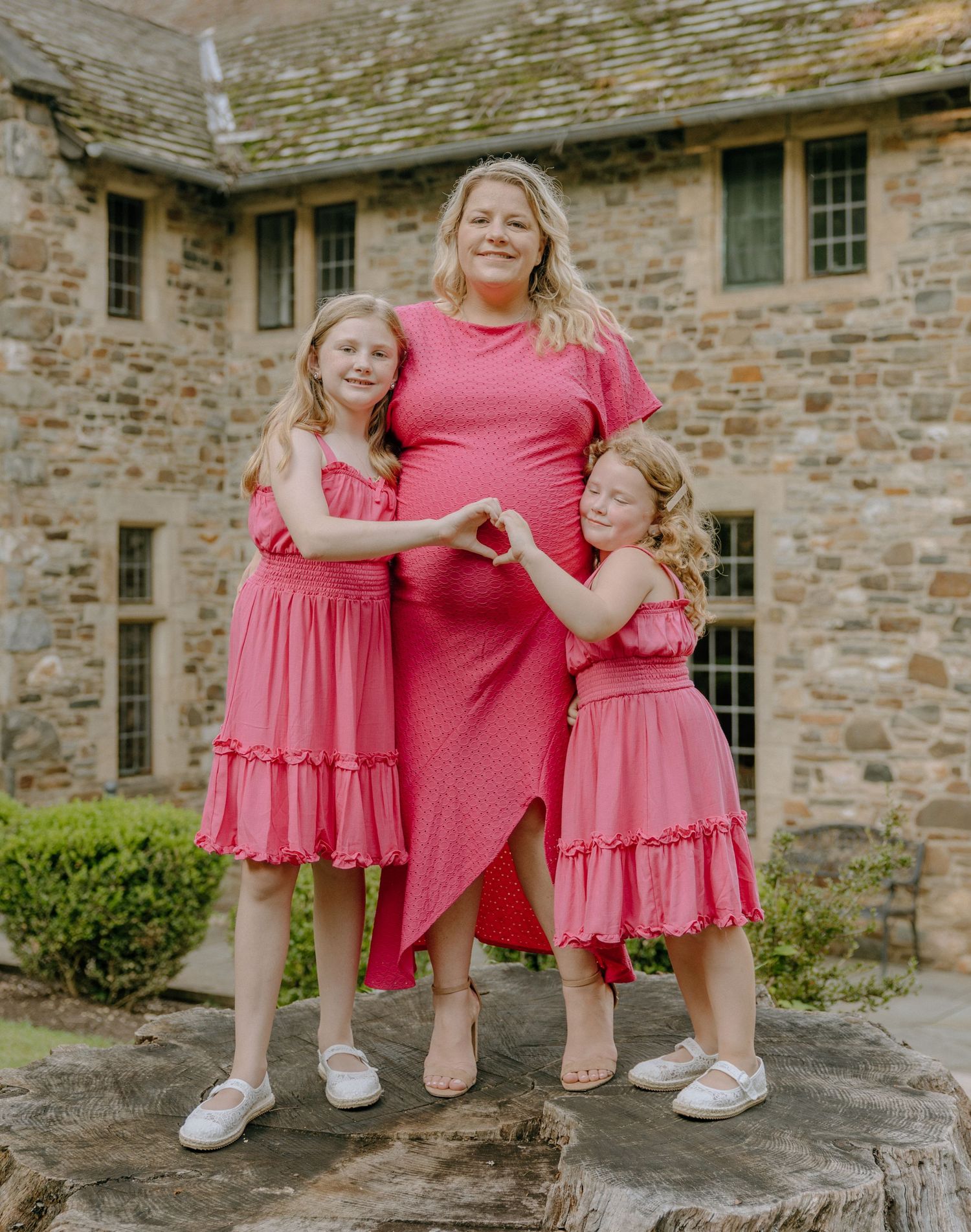 Family members in matching pink outfits pose casually on stone ledge near historic building.