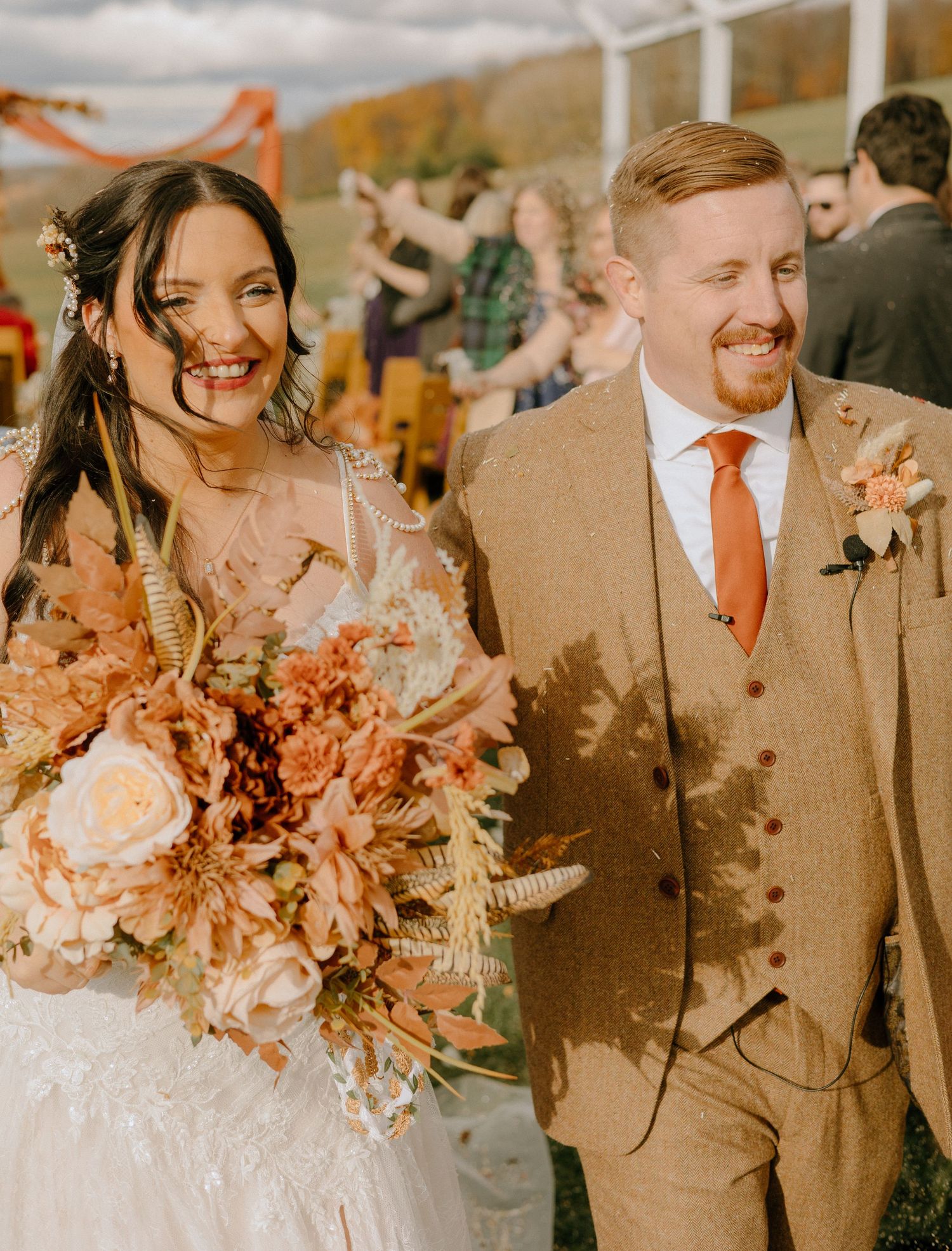 Wedding party in brown suits and flowing dress posing with coral-colored floral bouquets.