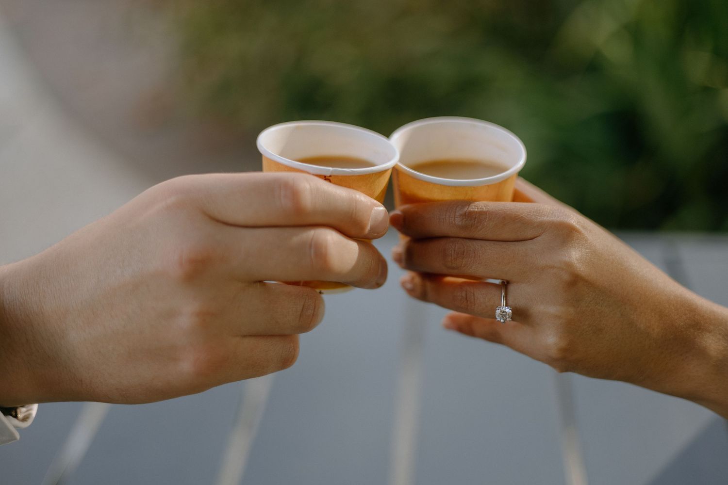 Two hands toasting with small espresso cups against a blurred green background.