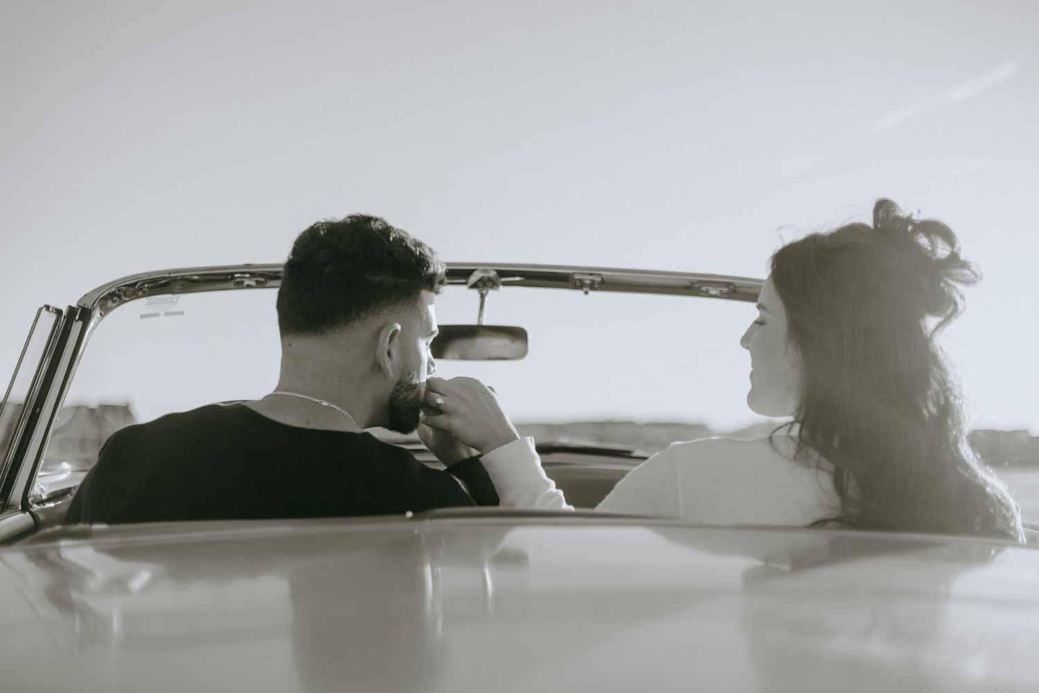 Silhouettes in a classic car against a bright sky creating a nostalgic mood.