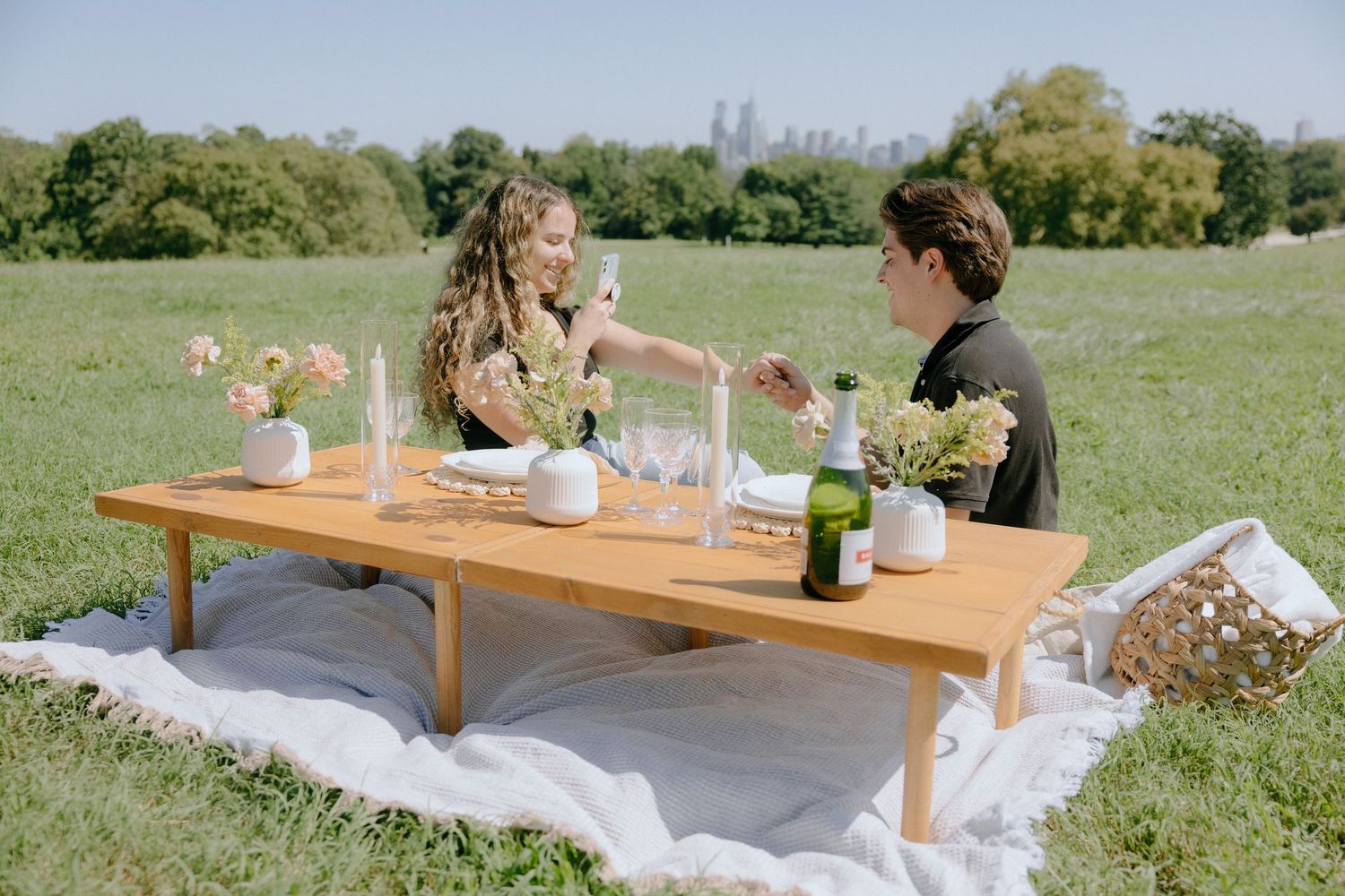 A romantic outdoor picnic setup with a low wooden table and white blanket on grass.