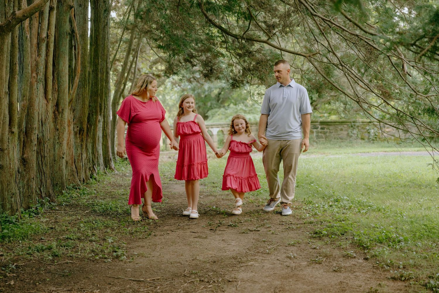 Family walking together on a tree-lined path wearing coordinated pink and gray outfits.