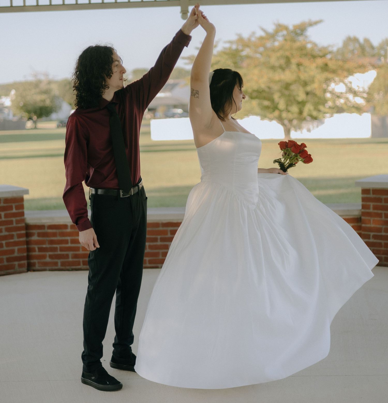 A couple in wedding attire dances together on an outdoor patio with arms raised.