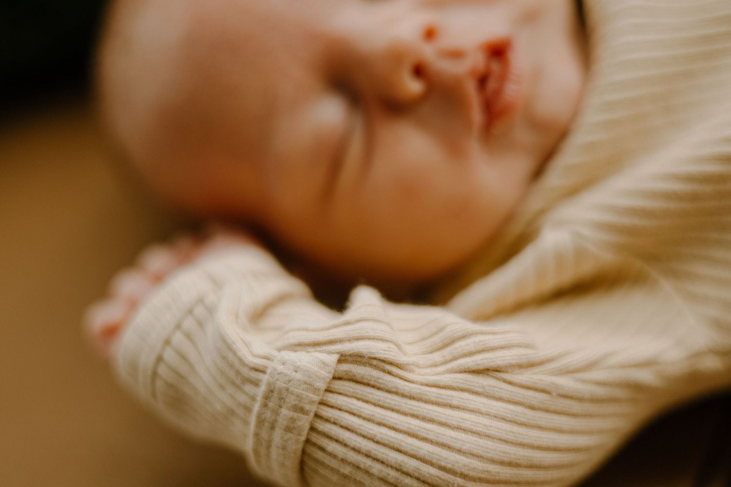 A baby rests peacefully on white bedding while wearing a cozy knit sweater.