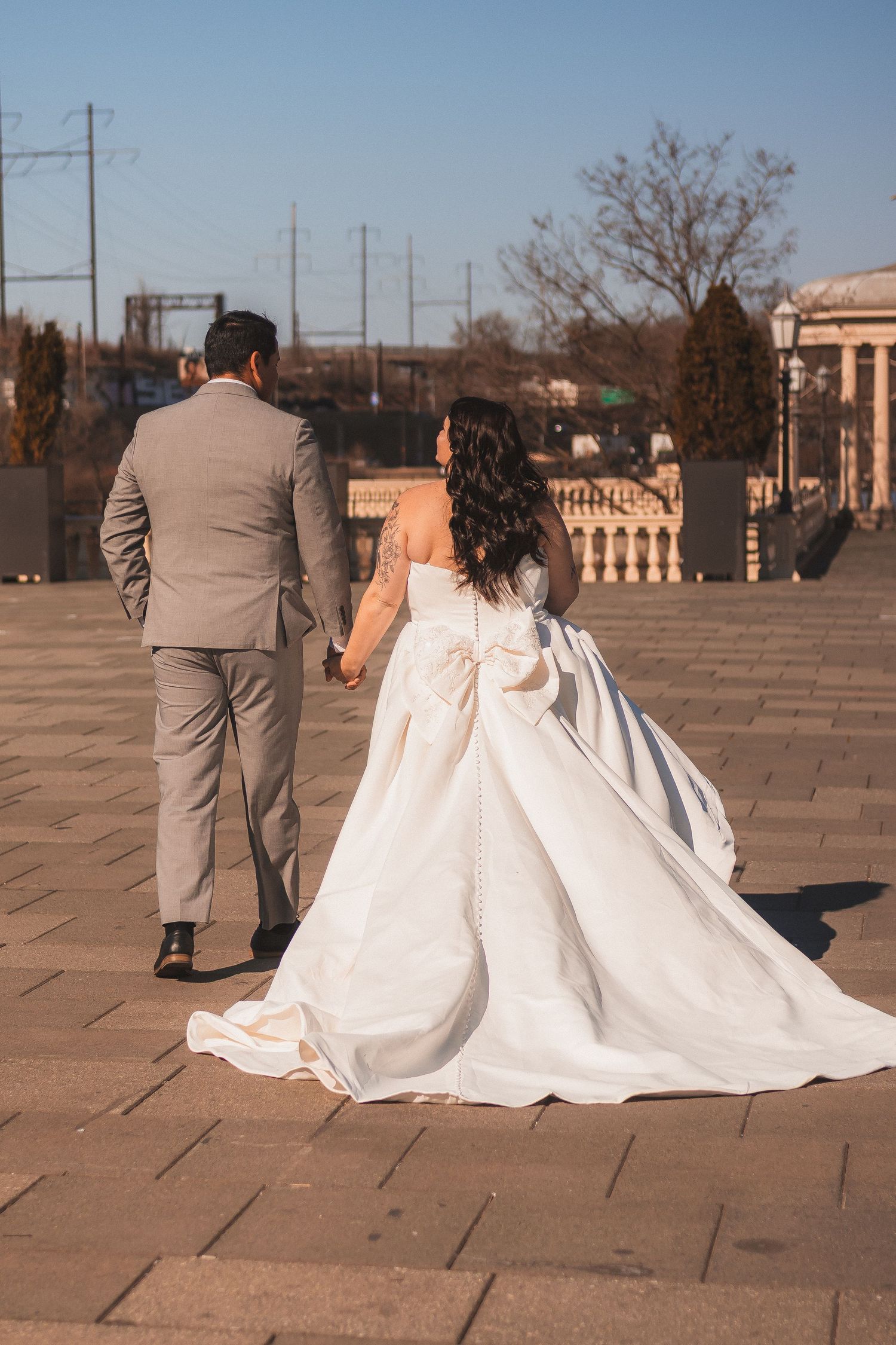 Wedding couple walking on stone pavement with bride's white dress trailing beautifully behind.