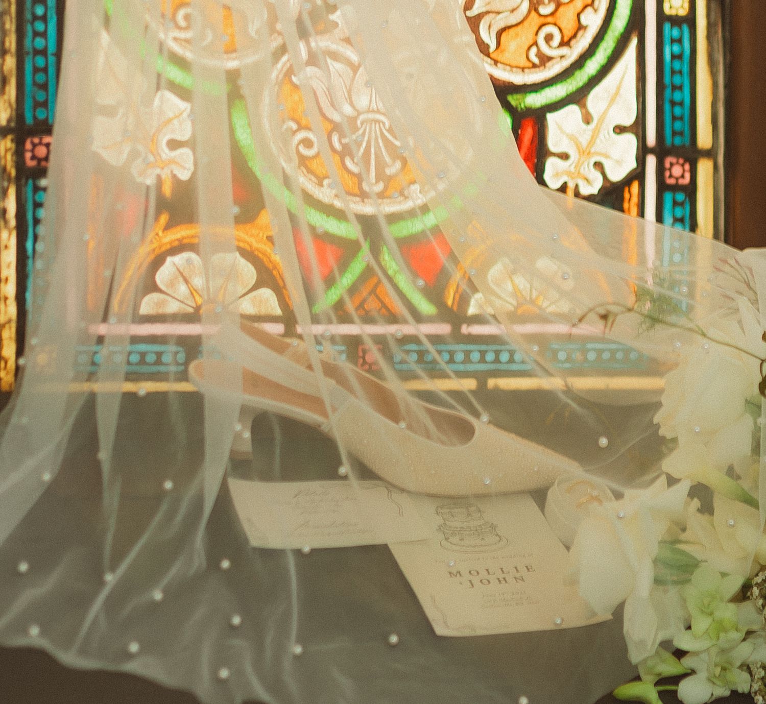 White bridal shoes displayed against decorative stained glass window background.